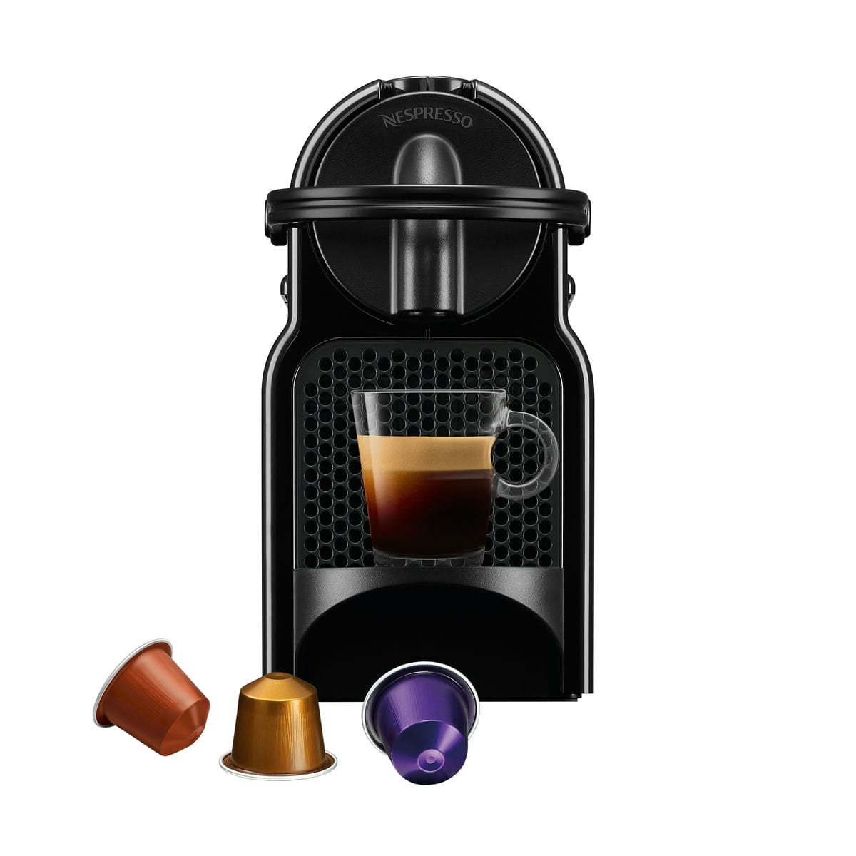 Czarny ekspres do kawy Nespresso z filiżanką kawy. Poniżej znajdują się trzy kapsułki z kawą. Maszyna ma kratkową konstrukcję.