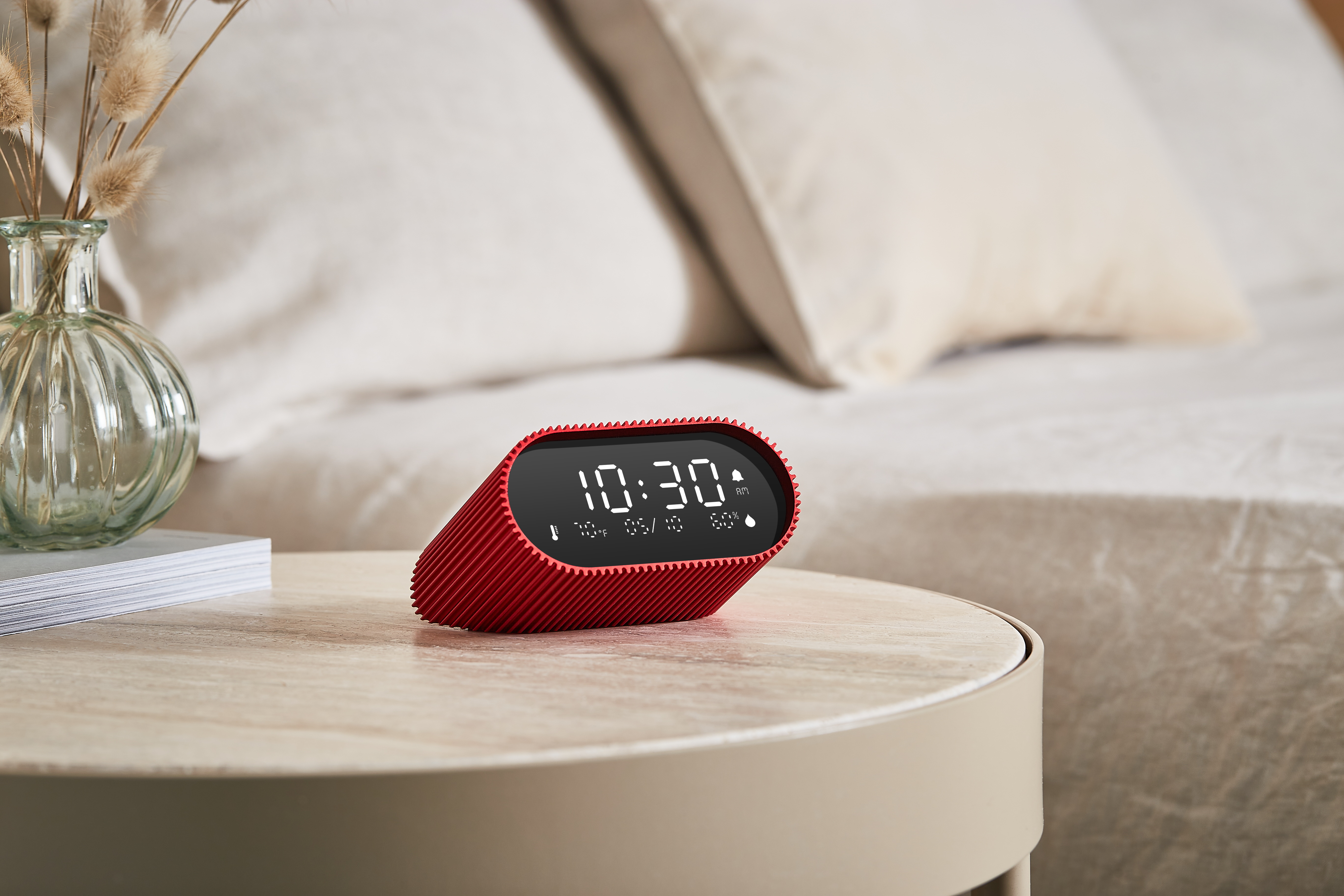 Eine rote Digitaluhr auf einem beigen Tisch zeigt 10:30 Uhr an, mit einer Vase und einem Bett im Hintergrund.