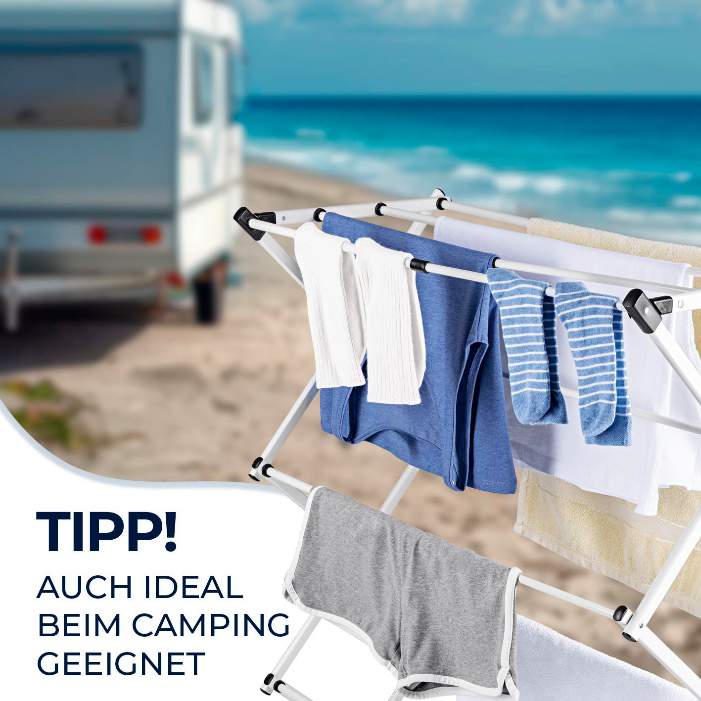 Wäscheständer mit weißer, blauer und gestreifter Kleidung an einem Strand mit einem Wohnmobil im Hintergrund.