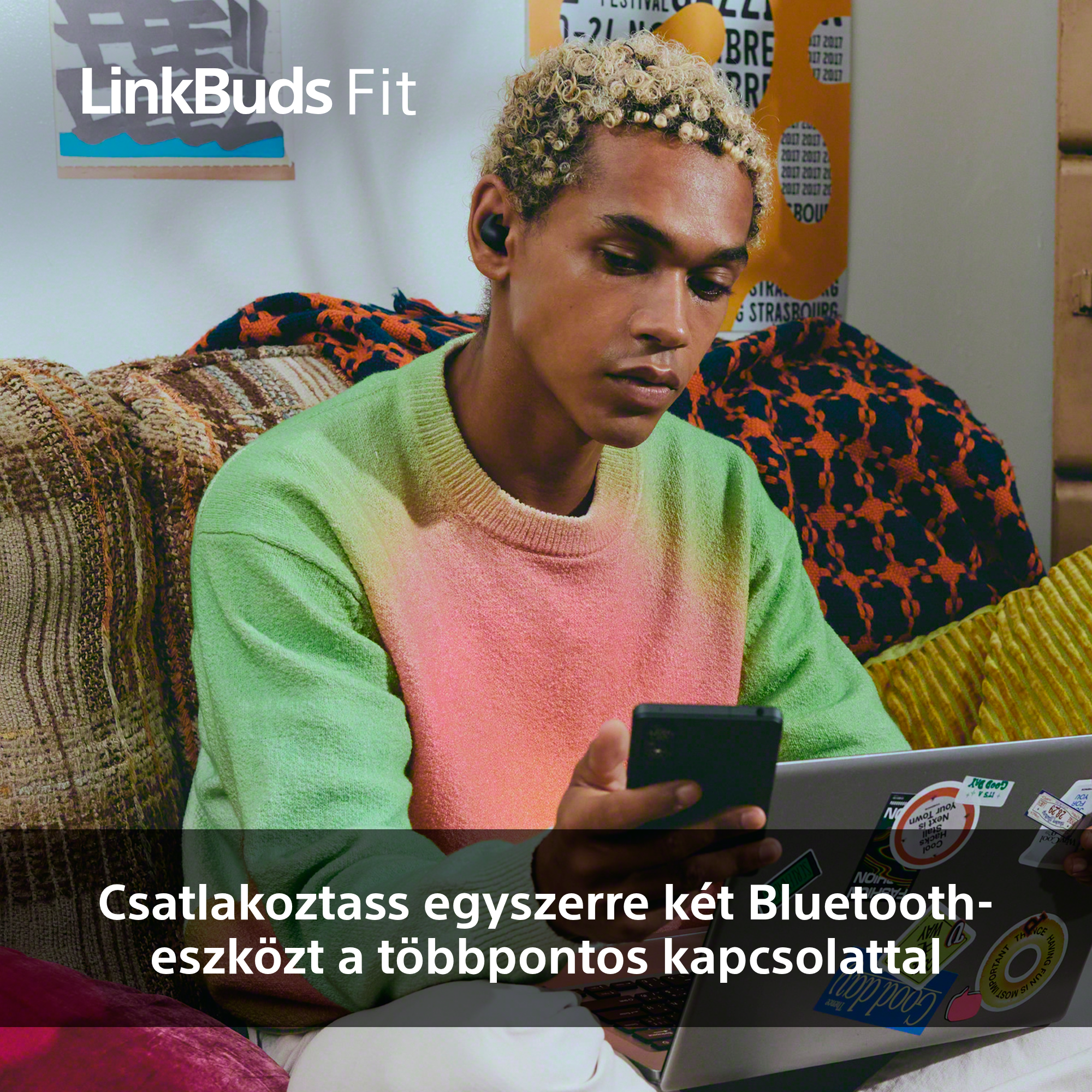 Egy fülhallgatós személy telefont tart, egy laptop előtt ül. Színes párnák vannak a háttérben.