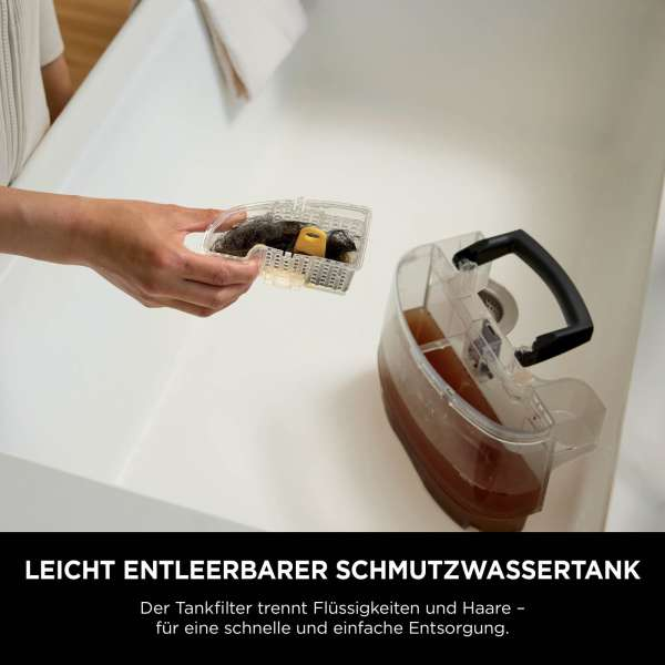 Eine Hand hält einen Filter mit Ablagerungen, neben einem Tank mit brauner Flüssigkeit. Der Tank hat einen schwarzen Griff. Weißer Hintergrund.