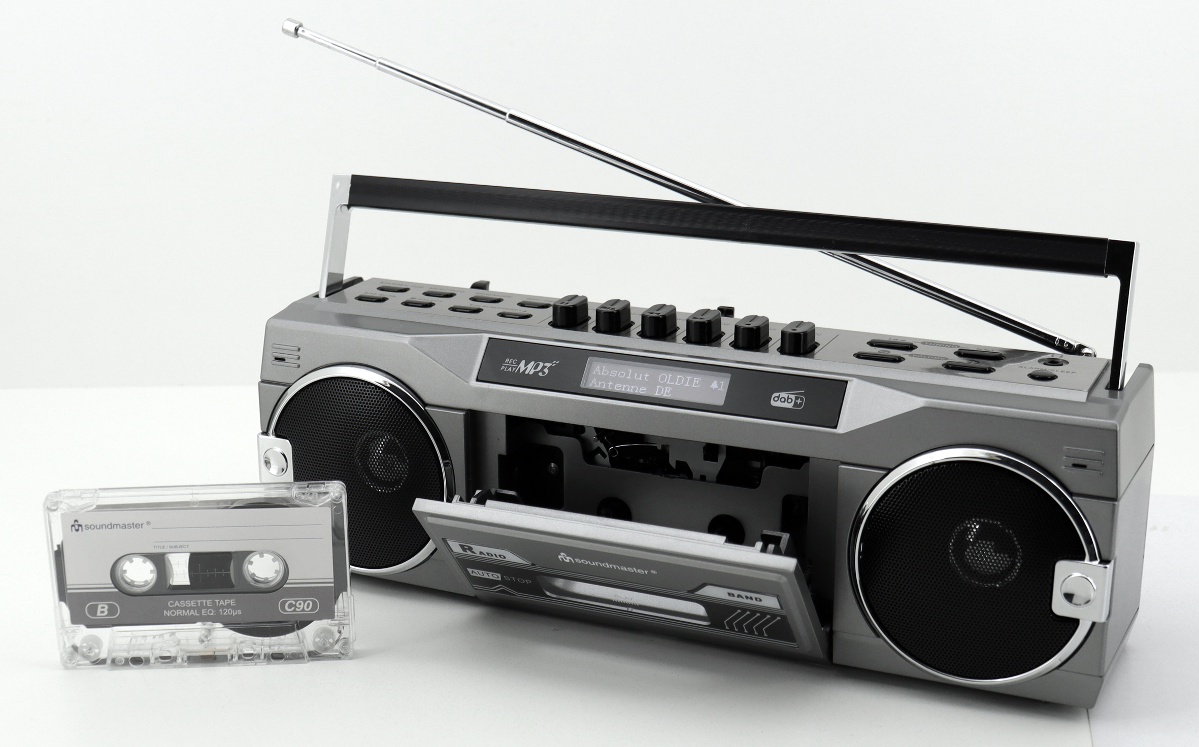 Ein grauer Ghettoblaster mit Kassette und Radioantenne. Die Kassettentür ist geöffnet. Die Szene befindet sich auf einer weißen Oberfläche.