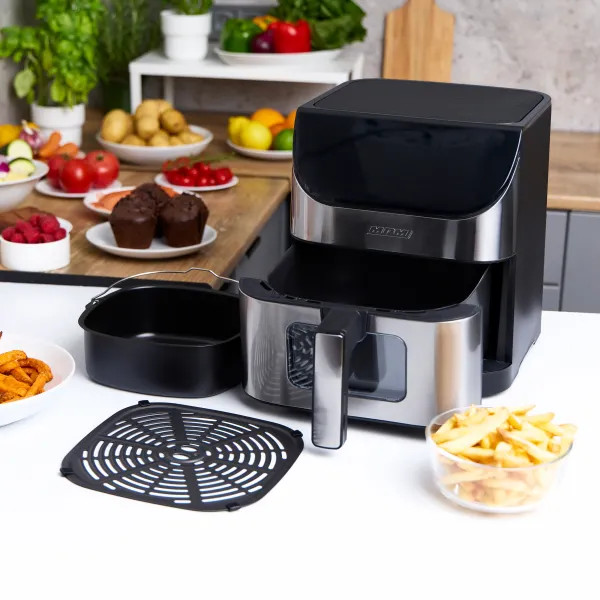 Frytownica powietrzna z akcesoriami stoi na blacie. W pobliżu znajdują się takie produkty jak muffiny, ziemniaki i frytki. Świeże produkty w tle.