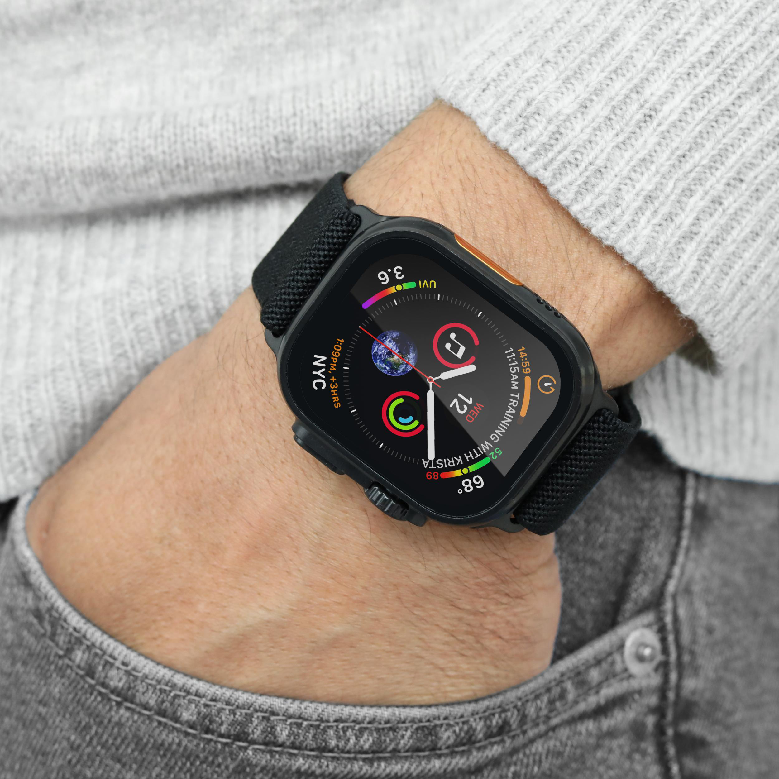 Eine Person, die eine schwarze Smartwatch am Handgelenk trägt, neben einem grauen Pullover und Jeans. Die Uhr zeigt Informationen.