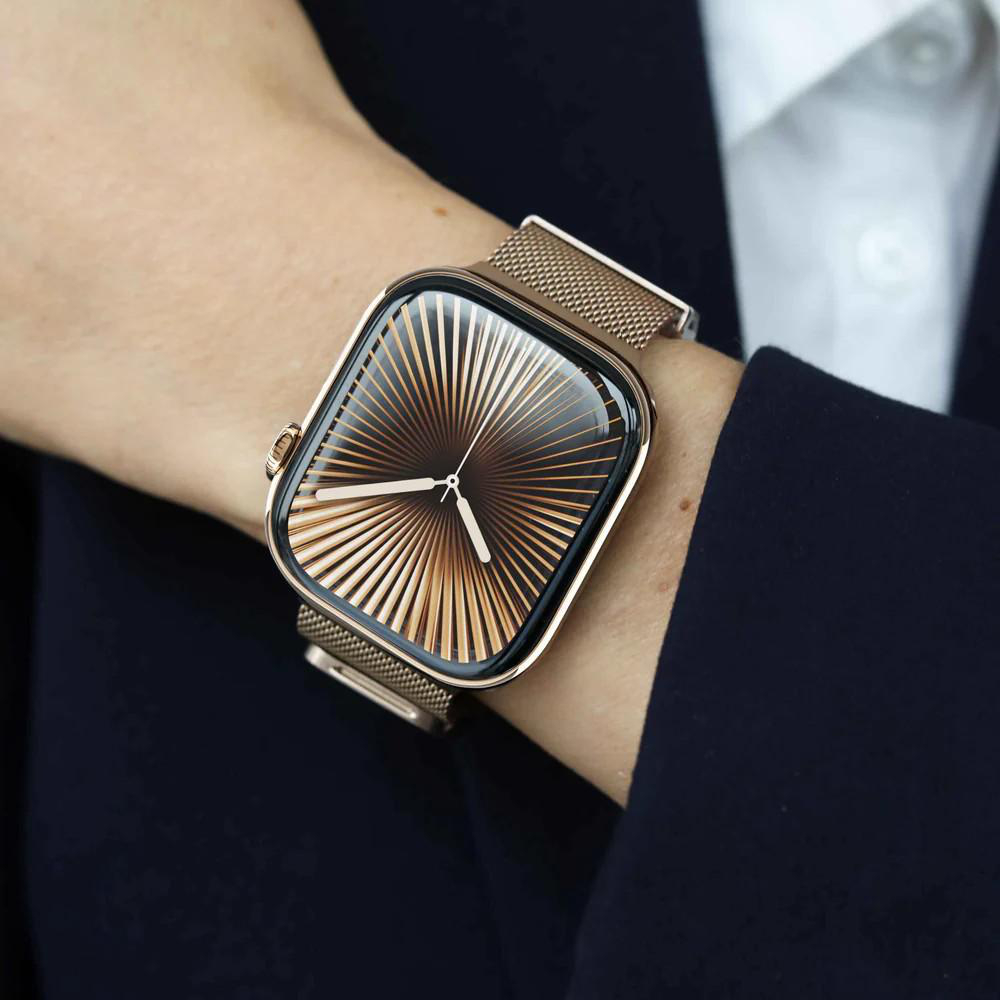 Eine Person trägt eine goldene Uhr. Das Zifferblatt hat ein radiales Design. Das Handgelenk befindet sich in der Nähe eines dunklen Blazers und eines weißen Hemdes.