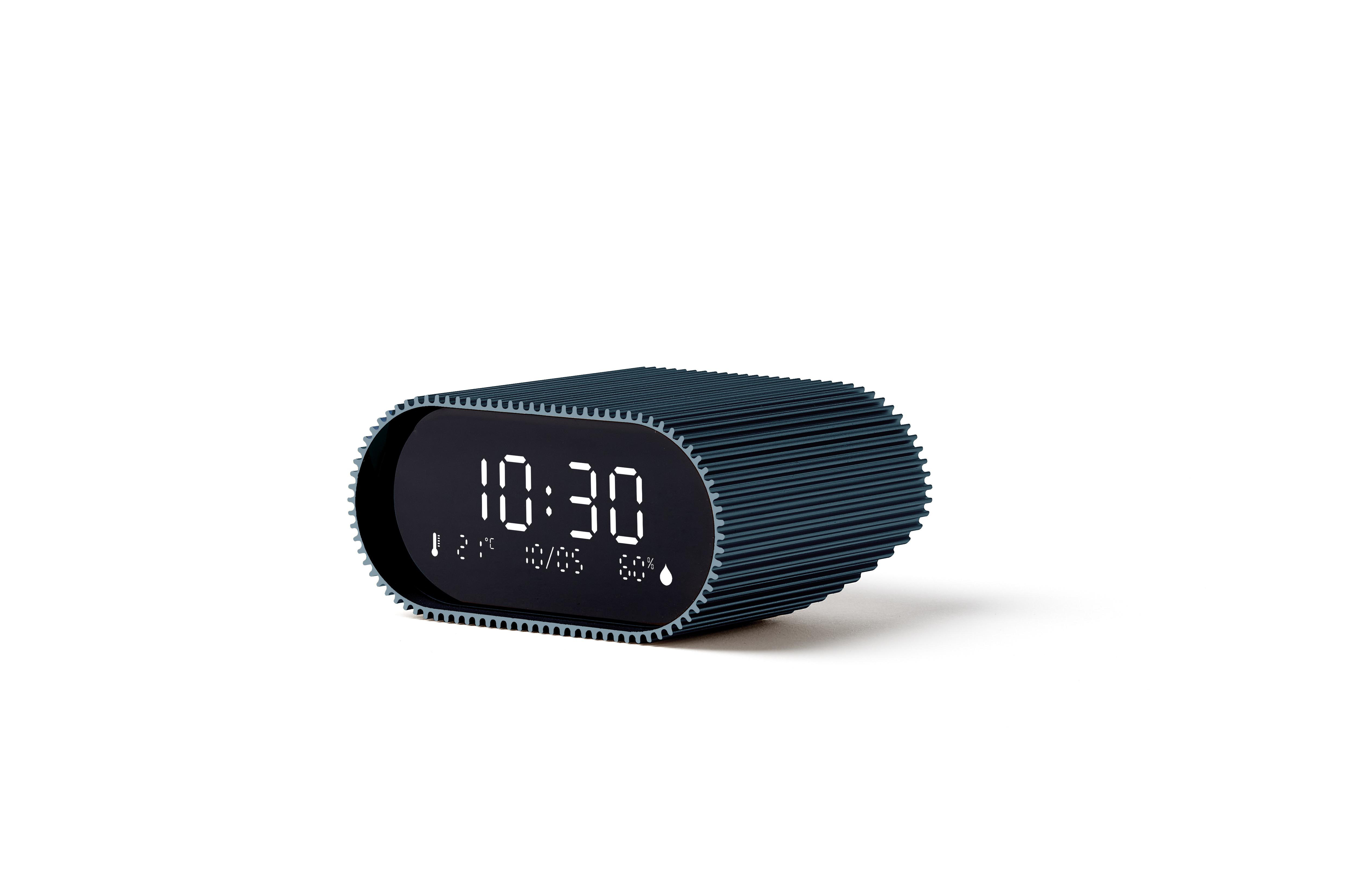 Eine ovalförmige Digitaluhr zeigt 10:30 Uhr an. Es hat einen blau-grauen geriffelten Rahmen. Der Hintergrund ist weiß.