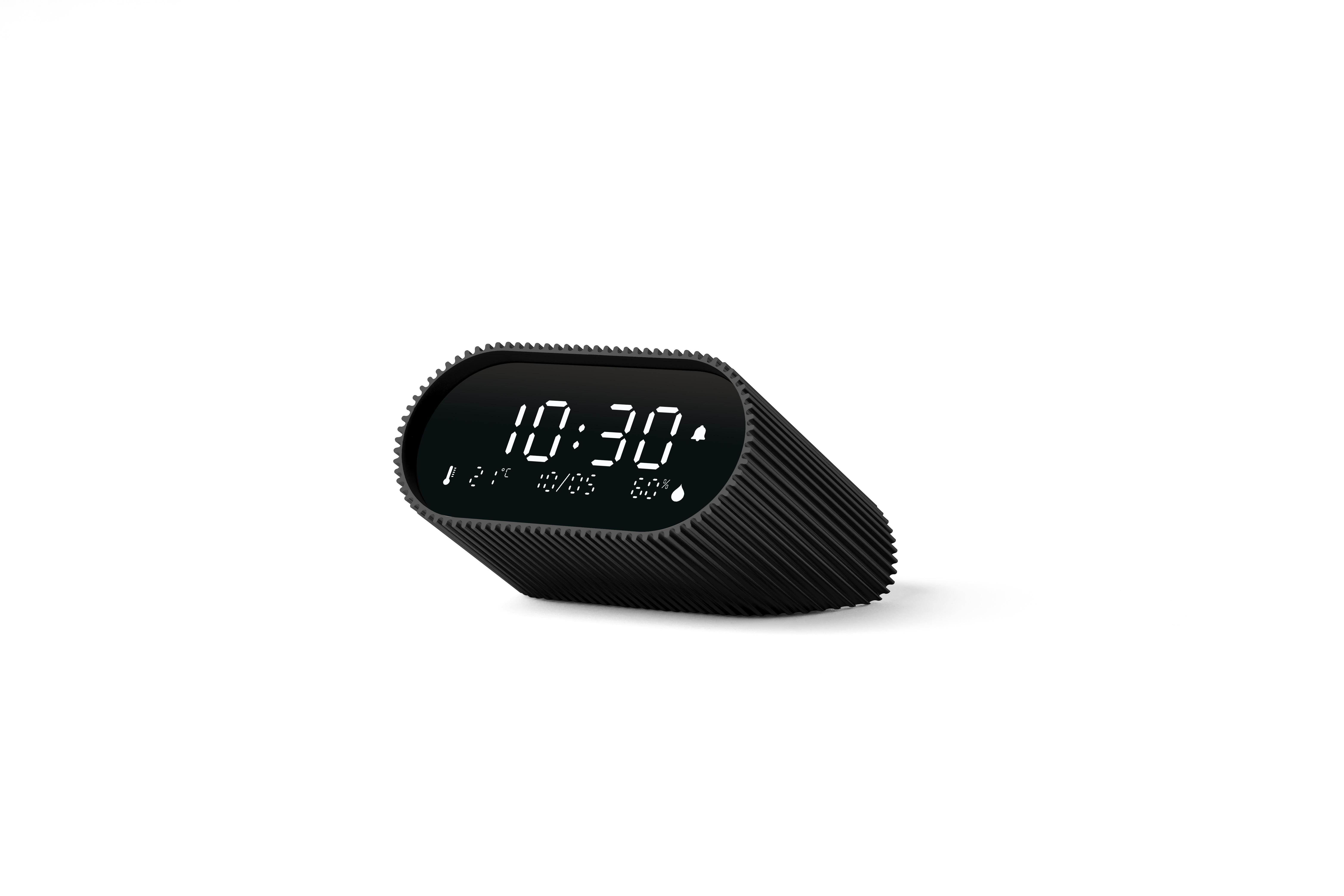 Eine schwarze Digitaluhr zeigt 10:30 Uhr an. Sie hat ein geripptes Design und steht auf weißem Grund.