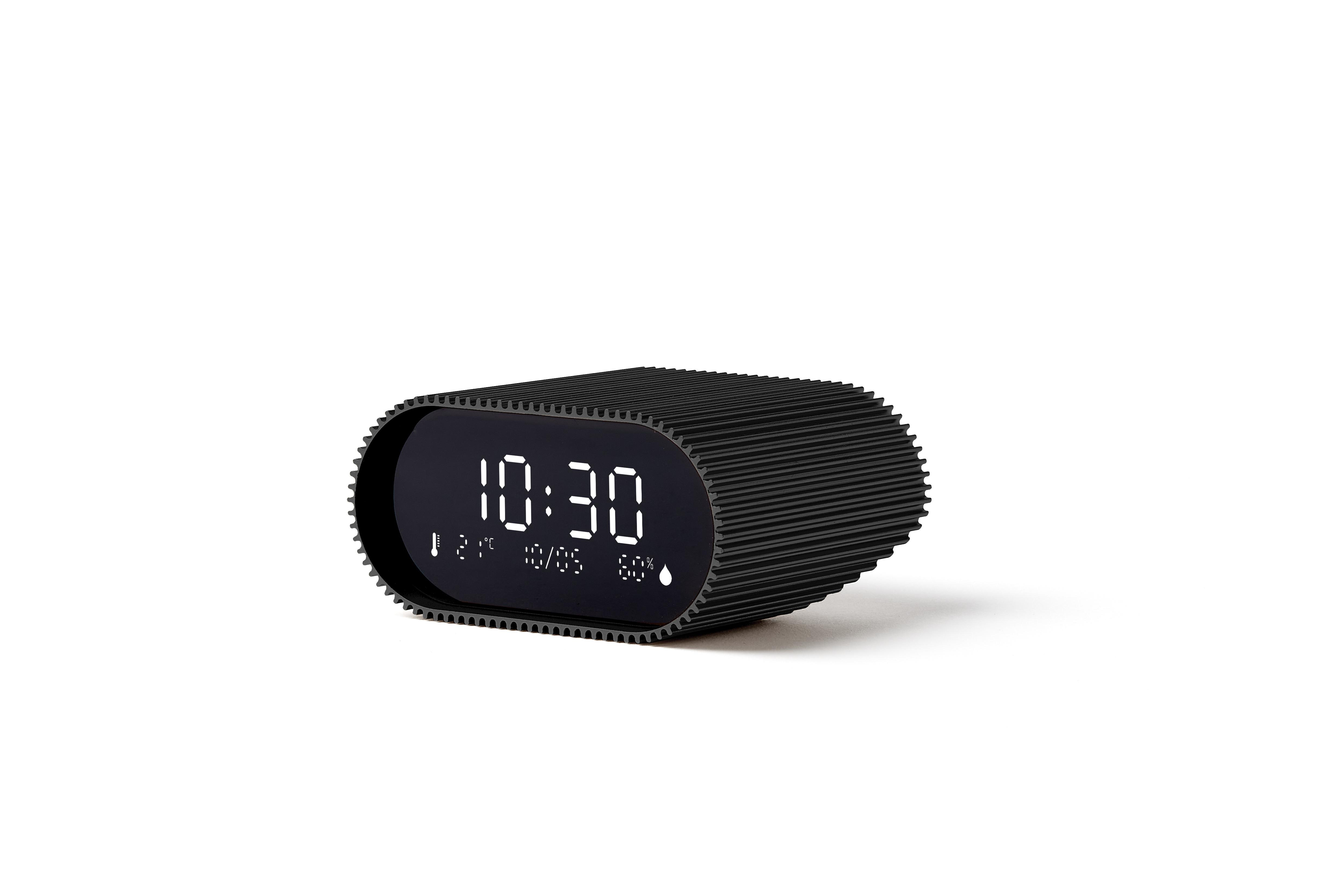 Eine schwarze Digitaluhr zeigt 10:30 Uhr an. Sie hat ein geripptes Design und steht auf weißem Untergrund.
