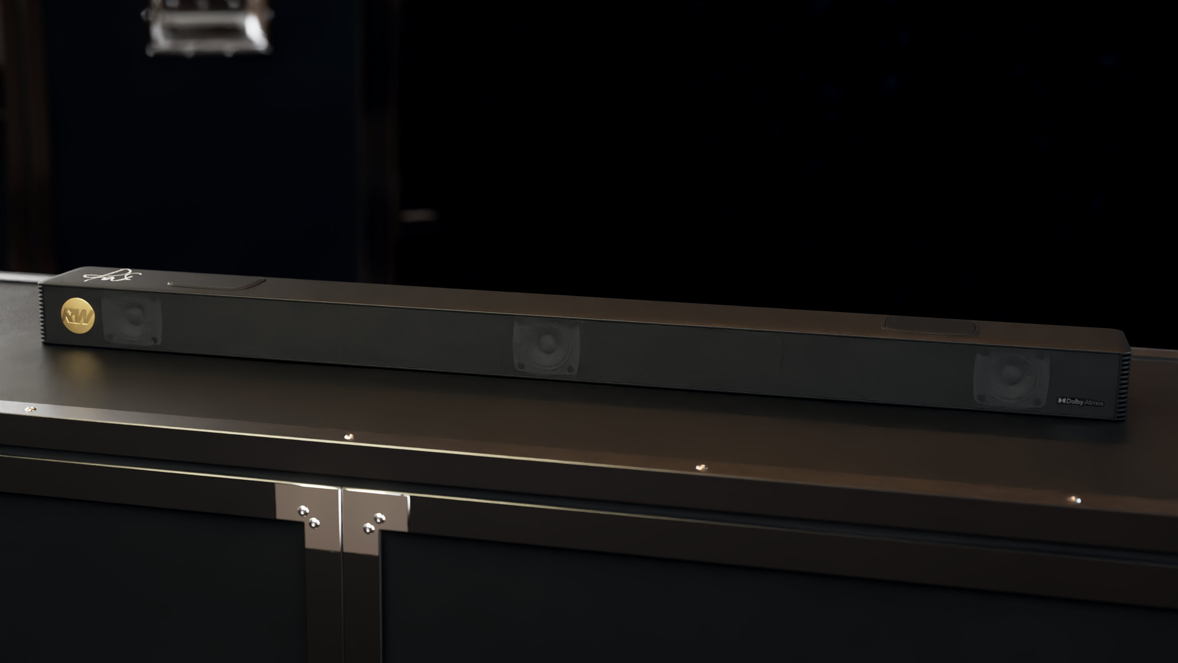 Czarny soundbar ze złotymi akcentami leży na ciemnej powierzchni. Tło jest ciemne, z rozmytym światłem górnym.