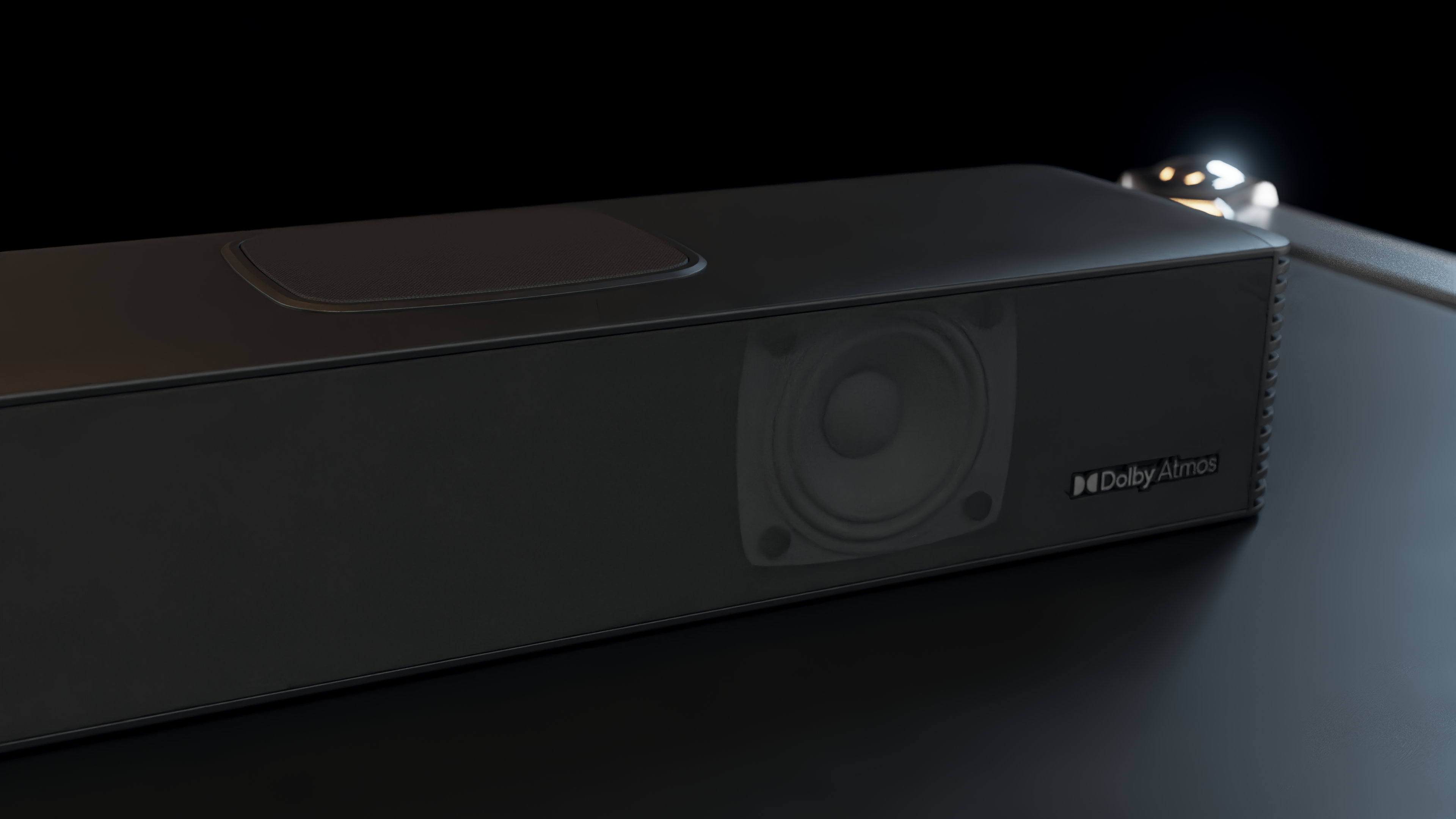 Czarny soundbar z głośnikiem i logo Dolby Atmos. Stoi na odblaskowej powierzchni, z ciemnym tłem.