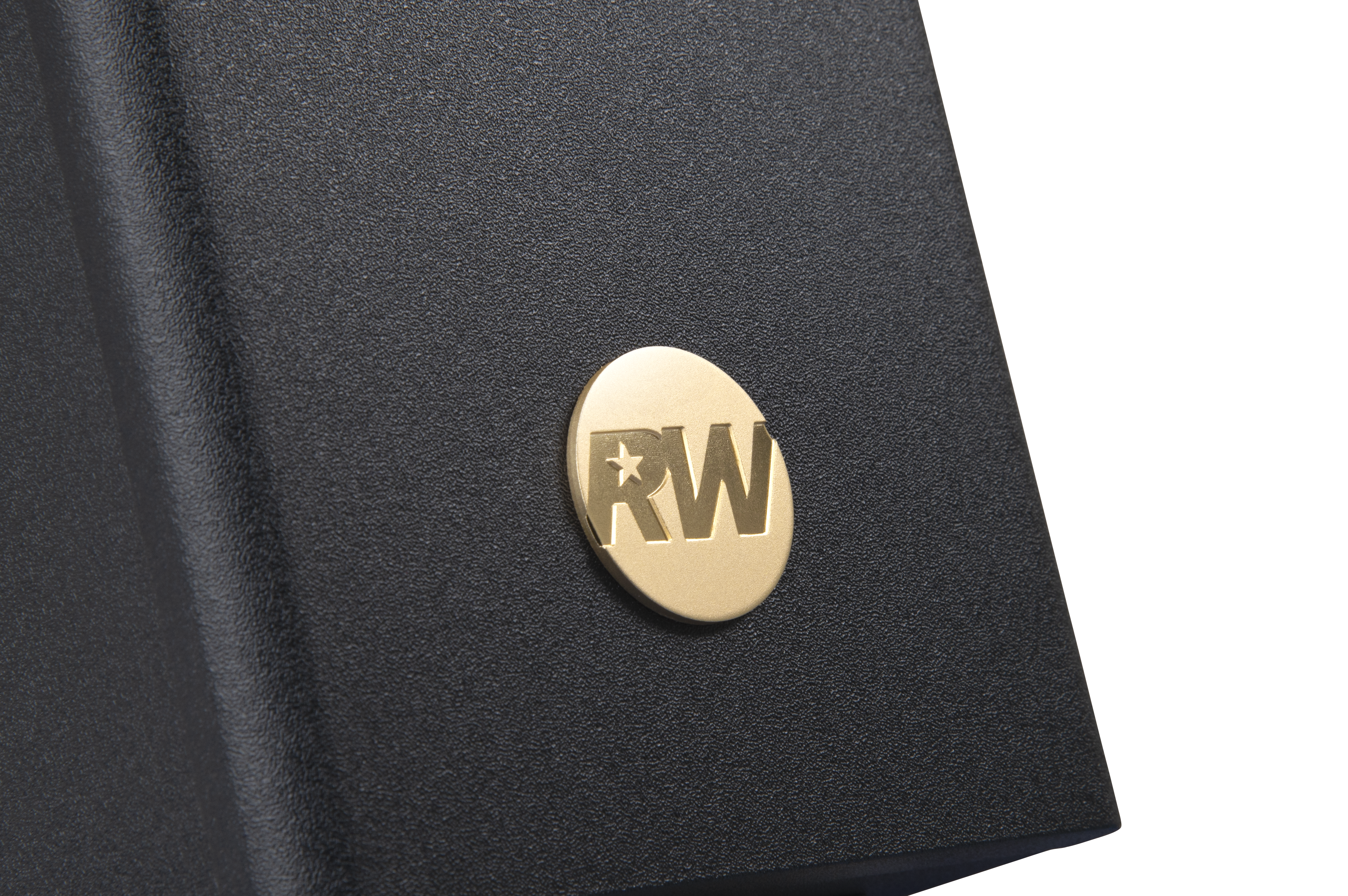 Zbliżenie pokazuje czarną, teksturowaną powierzchnię ze złotym, okrągłym emblematem. Emblemat ma litery 'RW' i gwiazdę.