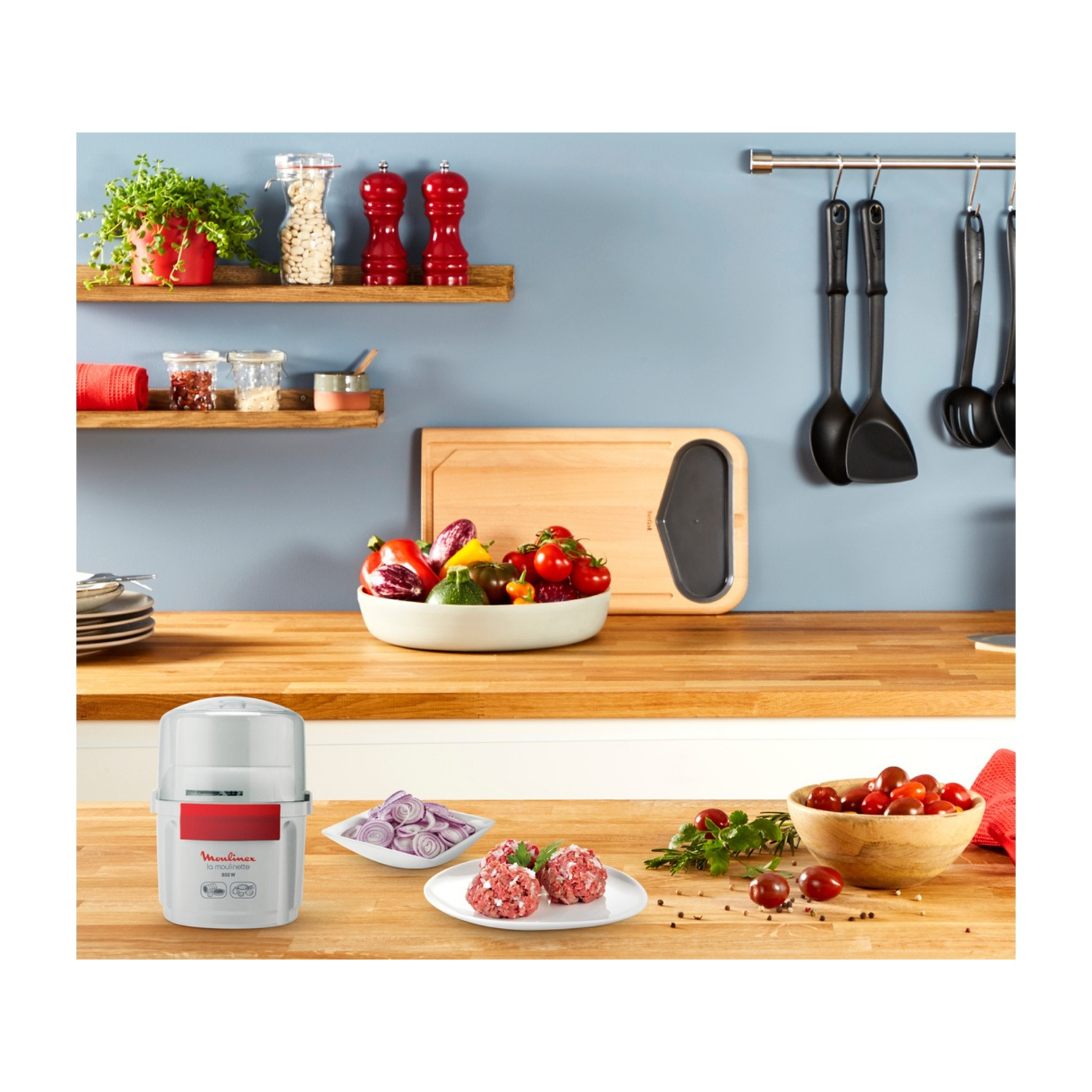 Una scena di cucina con verdure, erbe aromatiche e un robot da cucina. Gli ingredienti sono preparati su un piano di lavoro in legno, pronti per cucinare.