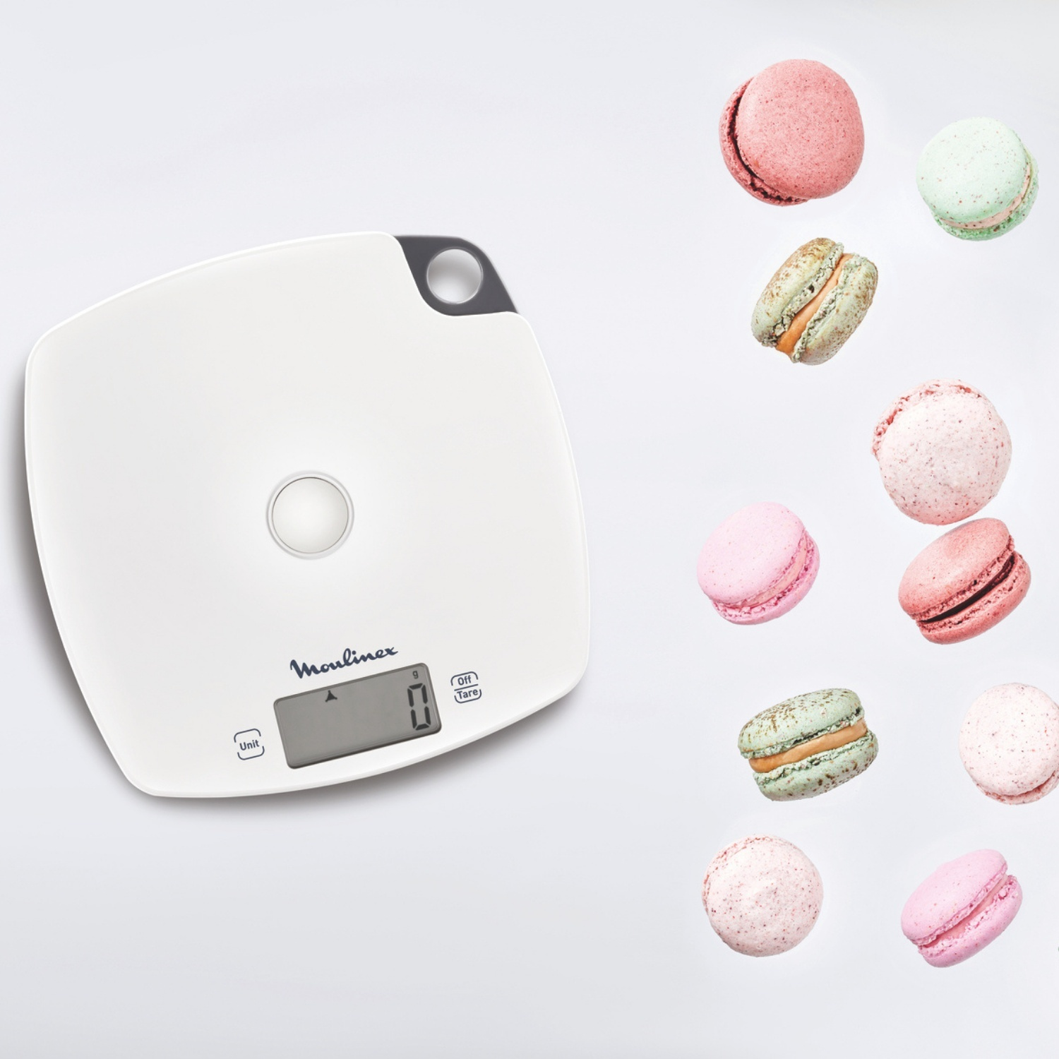 Una bilancia da cucina bianca con display digitale che mostra 0 g e diversi macarons colorati che fluttuano su sfondo bianco.