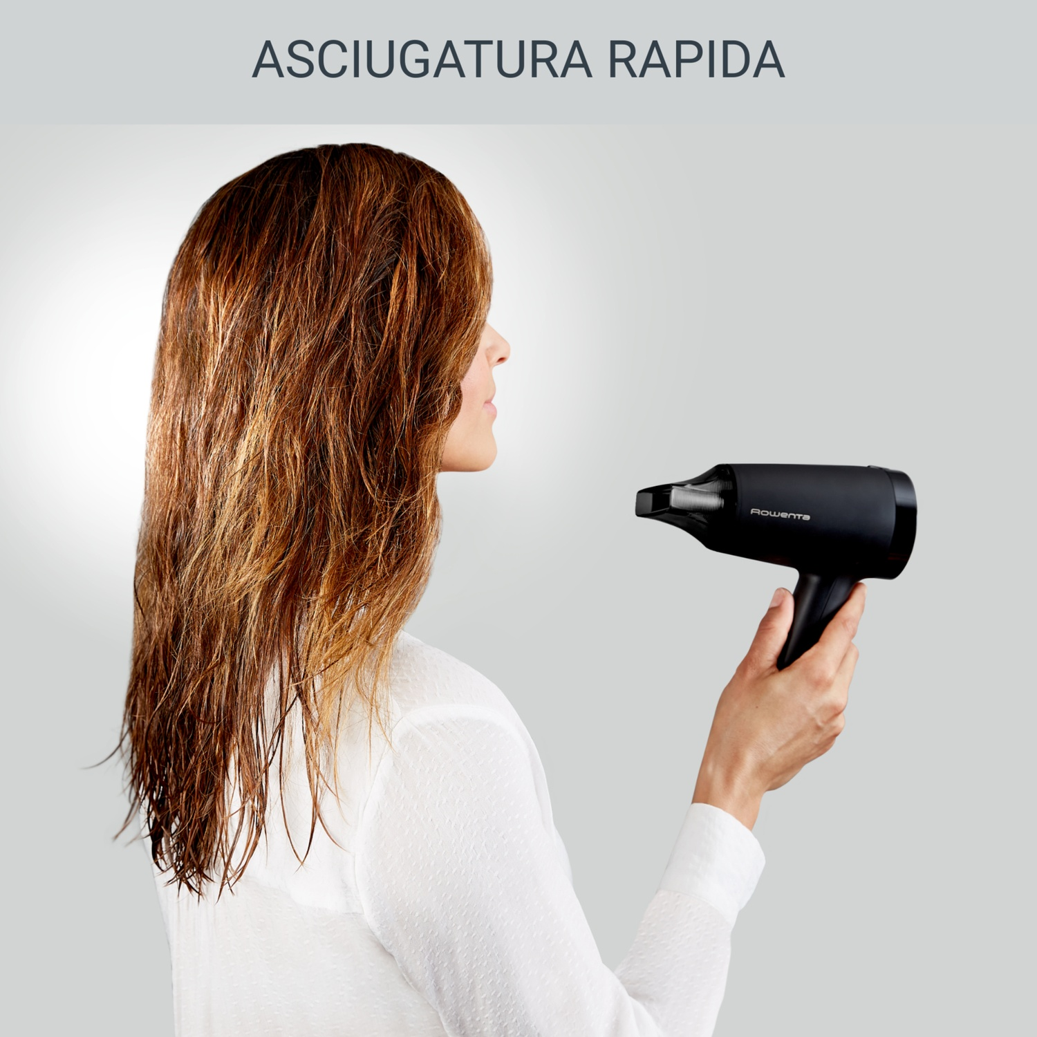 Una donna con capelli castani bagnati tiene un asciugacapelli nero. Lo sfondo è grigio chiaro e il testo dice 'Asciugatura rapida'.