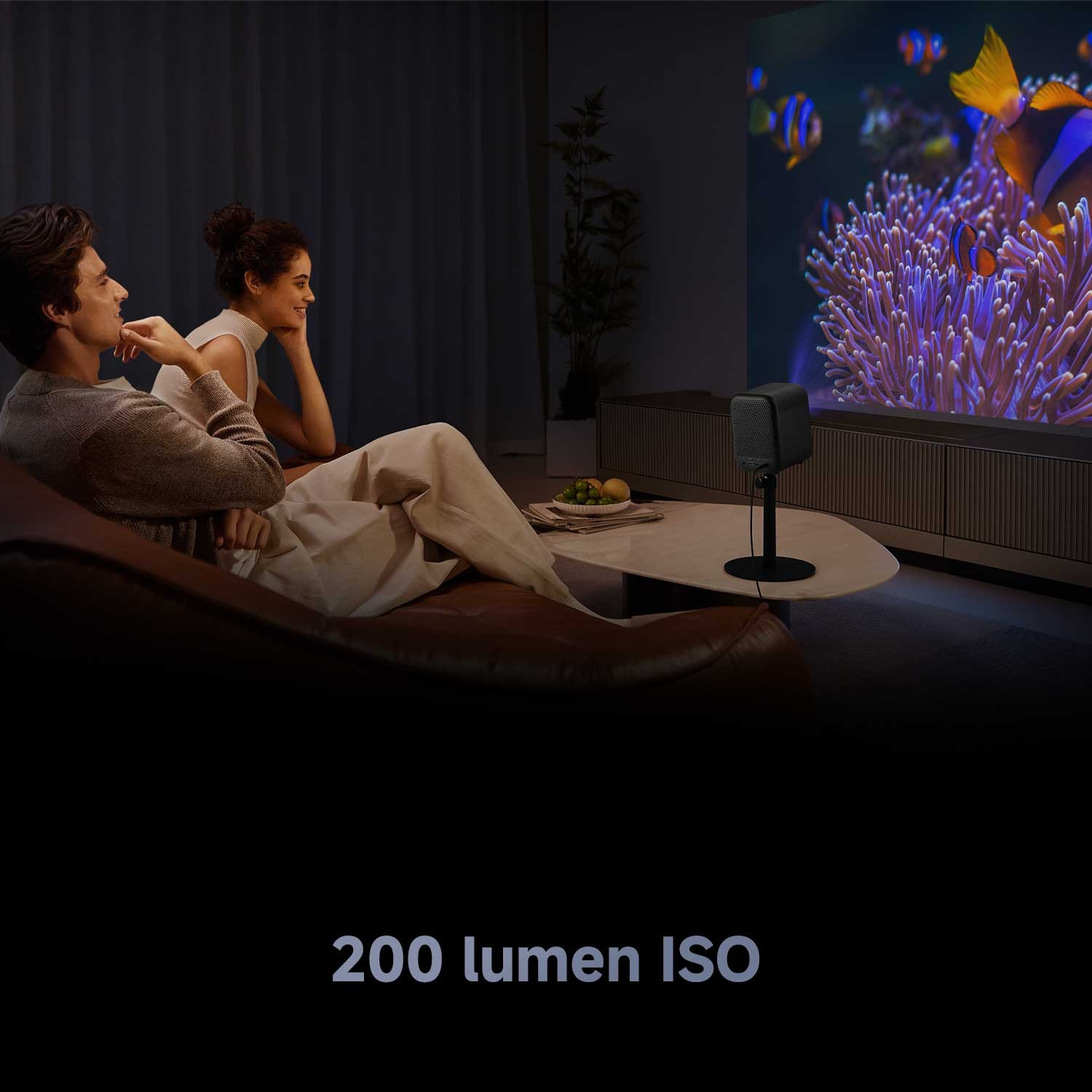 Una coppia guarda una scena di acquario proiettata. Un proiettore è su un supporto. Il testo dice 200 lumen ISO.