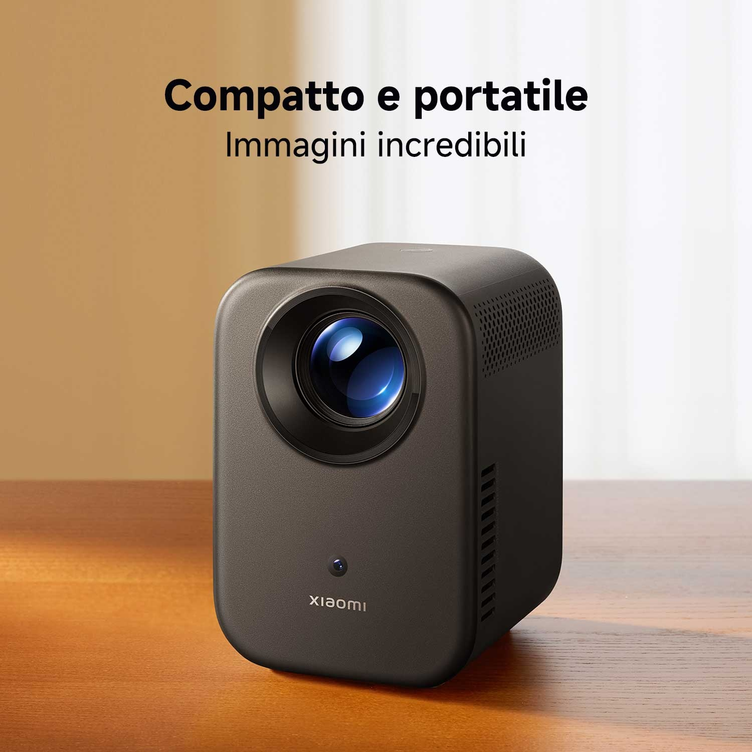 Un proiettore grigio scuro su una superficie di legno. Il proiettore ha una lente e il logo Xiaomi. Il testo in alto dice 'Compatto e portatile'.