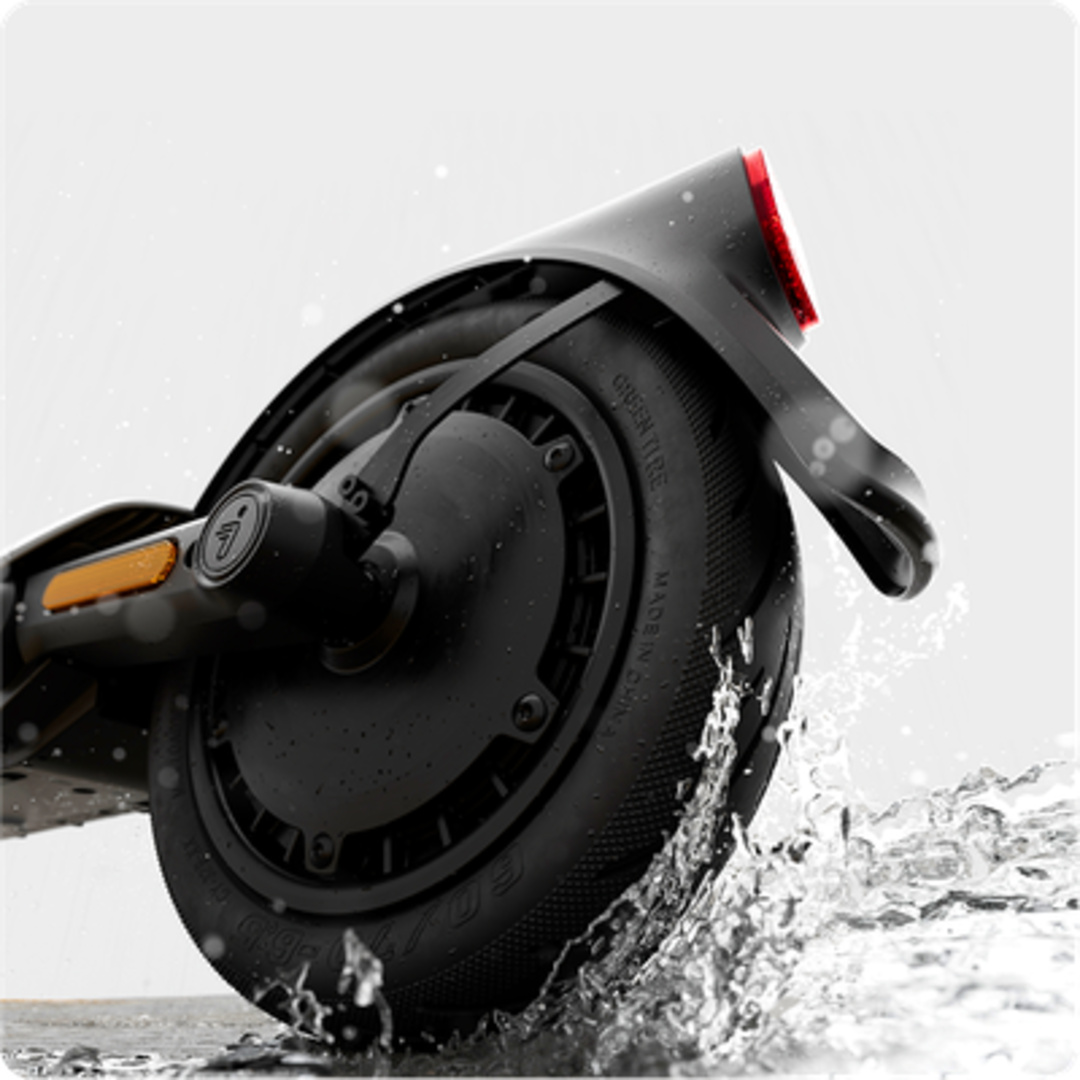 Roue noire de trottinette électrique avec éclaboussures. Le pneu est noir, avec le nom de la marque. L'eau éclabousse autour de la roue.