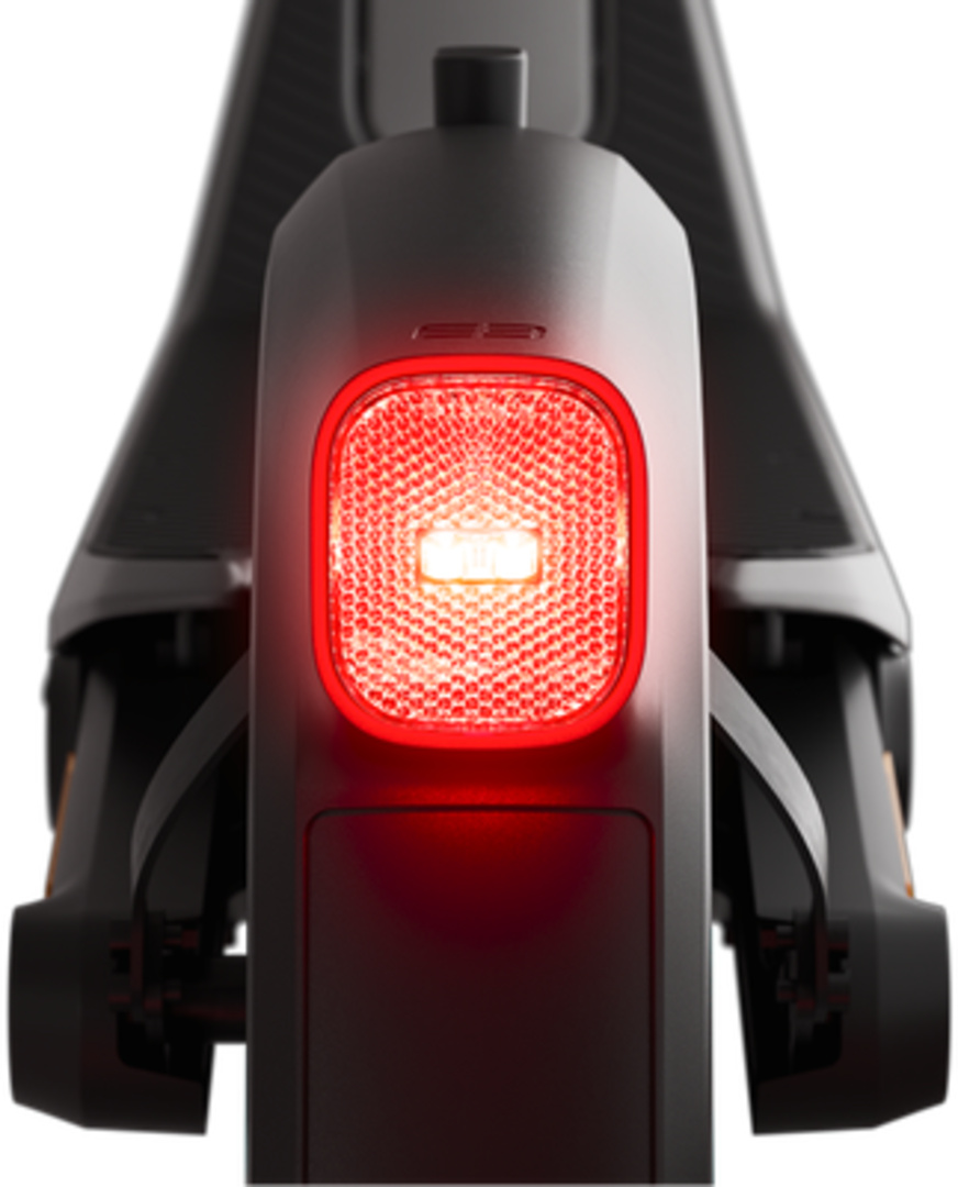 Arrière d'une trottinette noire avec un feu arrière rouge proéminent. Le feu arrière est rectangulaire, avec une surface texturée et un centre lumineux.