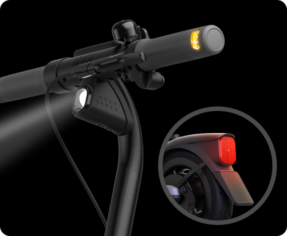 Gros plan sur le guidon d'une trottinette électrique. Il montre un phare avant, une sonnette et un clignotant orange. Un feu arrière rouge est également visible.