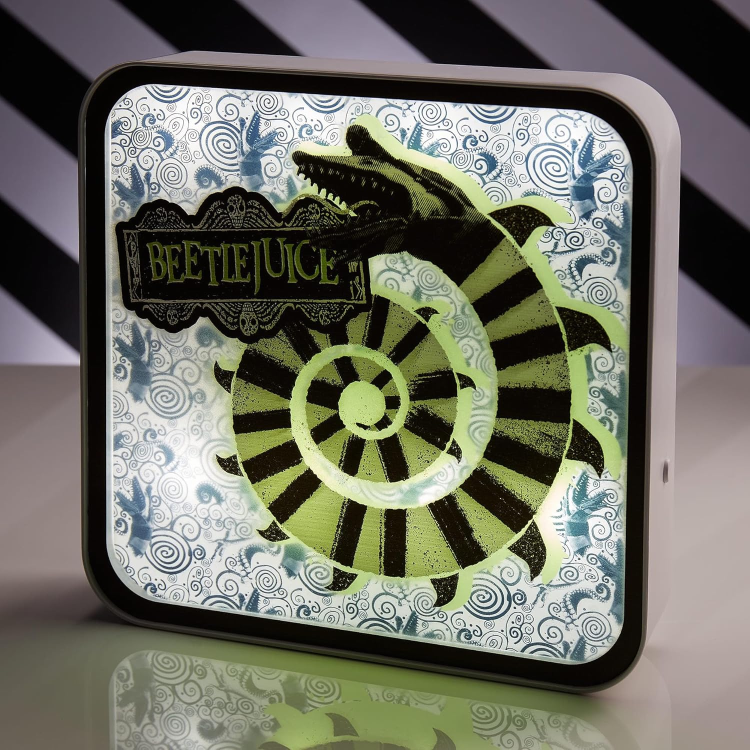 Megvilágított Beetlejuice felirat. Zöld-fekete csíkos spirál hüllőfejjel. A háttérben kék örvények és lények láthatók.