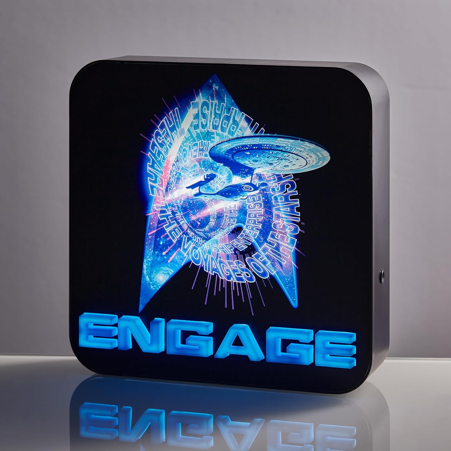 Star Trek tábla az Enterprise űrhajóval. Kék ragyogás az "ENGAGE" szóval alul. Fekete keret.
