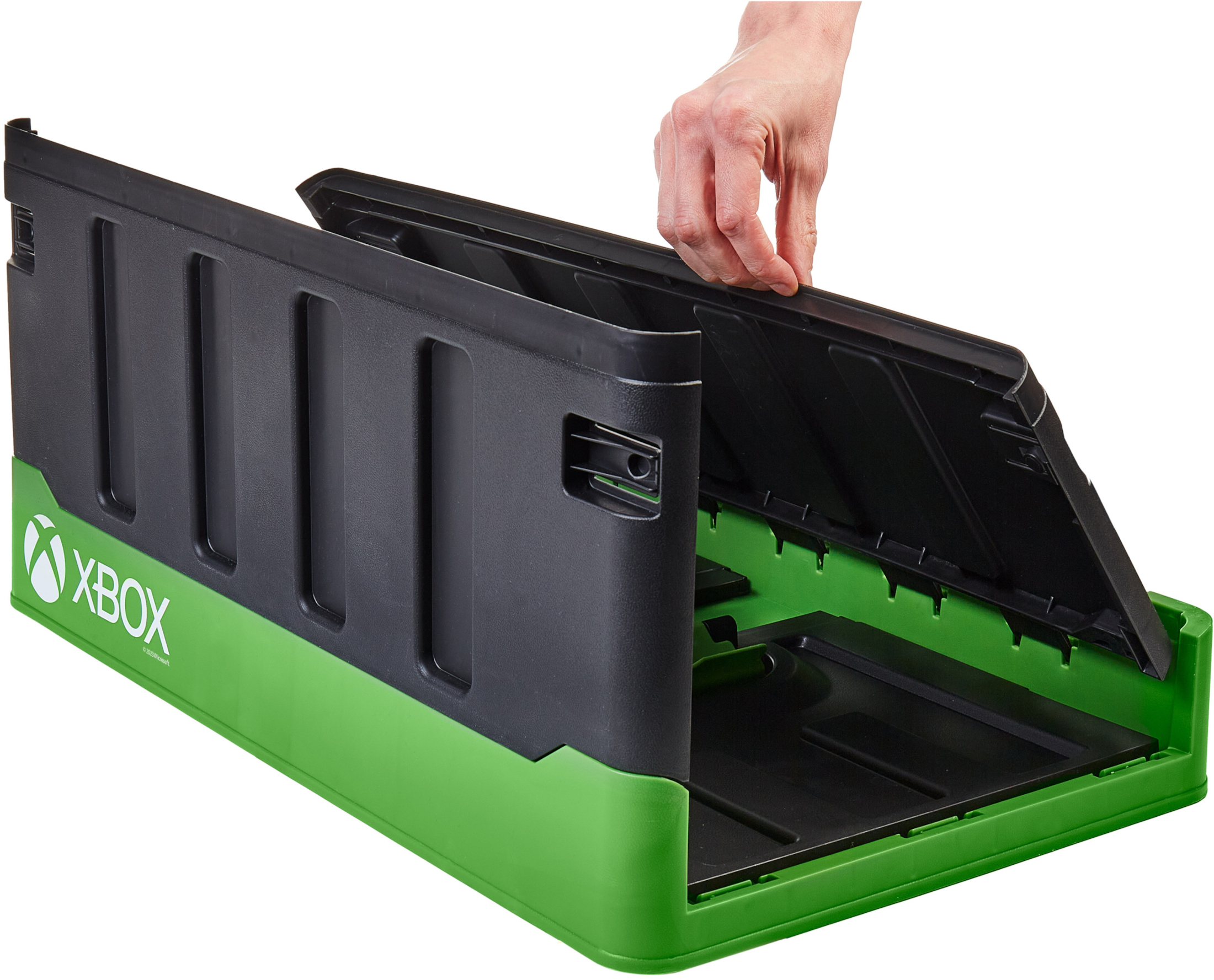 Egy Xbox márkájú tárolódoboz nyitva van. Egy kéz emeli fel a tetőt. A doboz fekete és zöld.