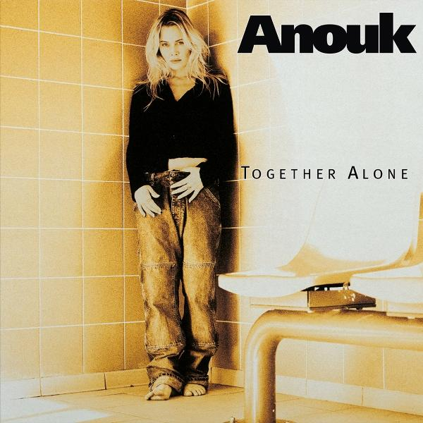 Blonde Frau in Jeans und schwarzem Oberteil steht an einer gefliesten Wand. Albumcover mit 'Anouk' und 'Together Alone'.