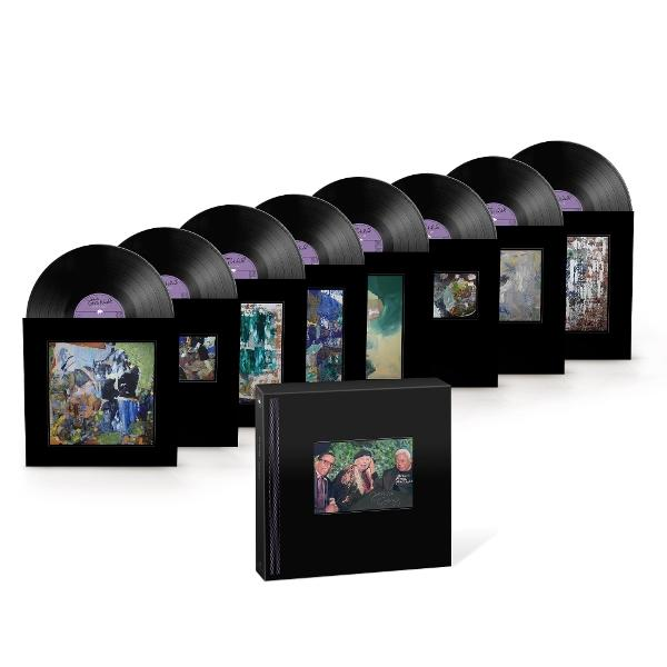 Sammlung von Vinylplatten in schwarzen Hüllen mit abstrakter Kunst. Ein Box-Set mit einem Foto von drei Personen befindet sich vorne.