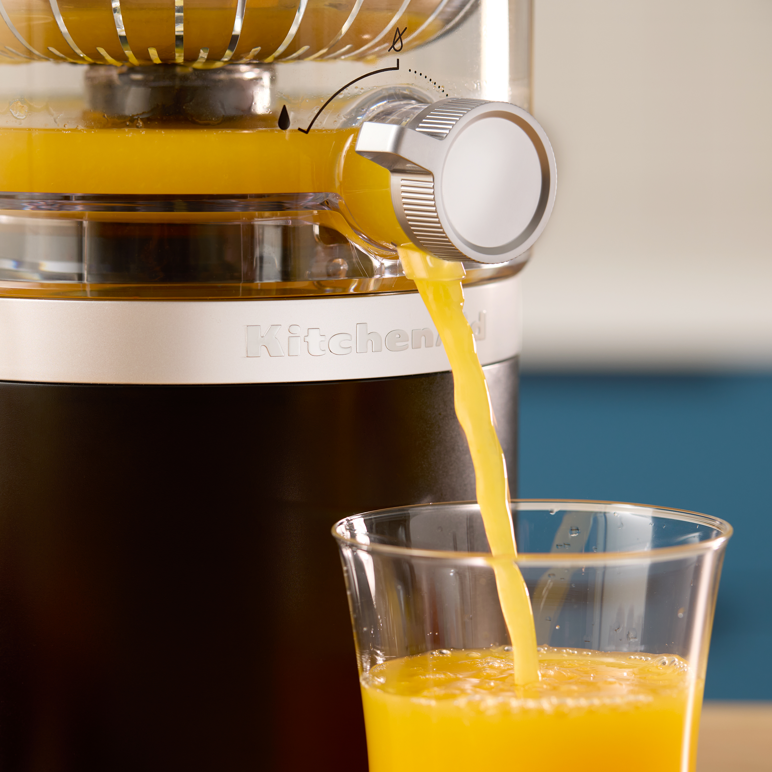 Ein Entsafter gibt frischen Orangensaft in ein Glas ab. Die Maschine ist schwarz und silberfarben. Der Hintergrund ist unscharf.