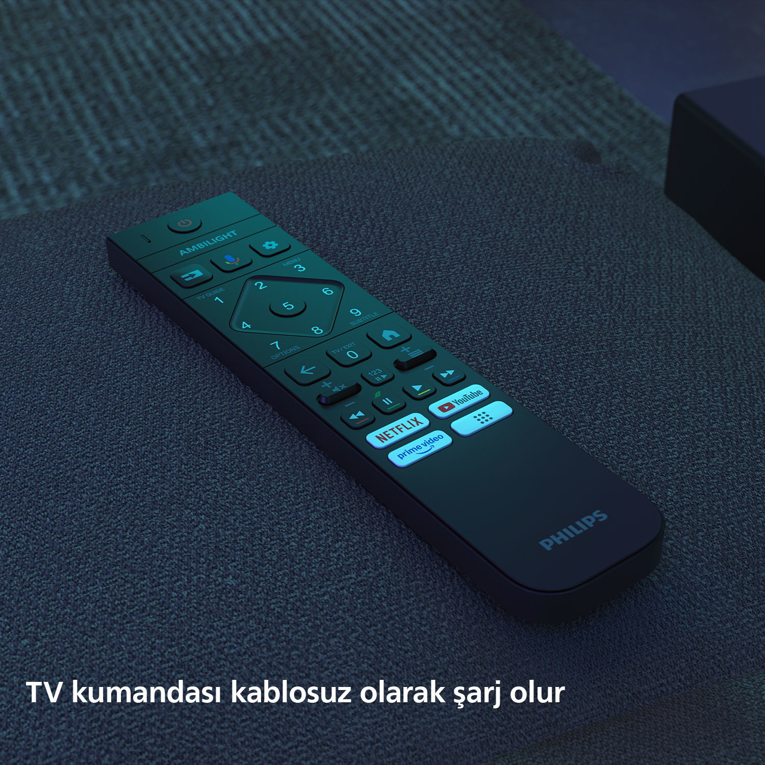 Gri kumaş üzerinde siyah Philips uzaktan kumandası. Netflix, YouTube ve sayı tuşları görülüyor. Metin: 'TV kumandası kablosuz şarj olur'.