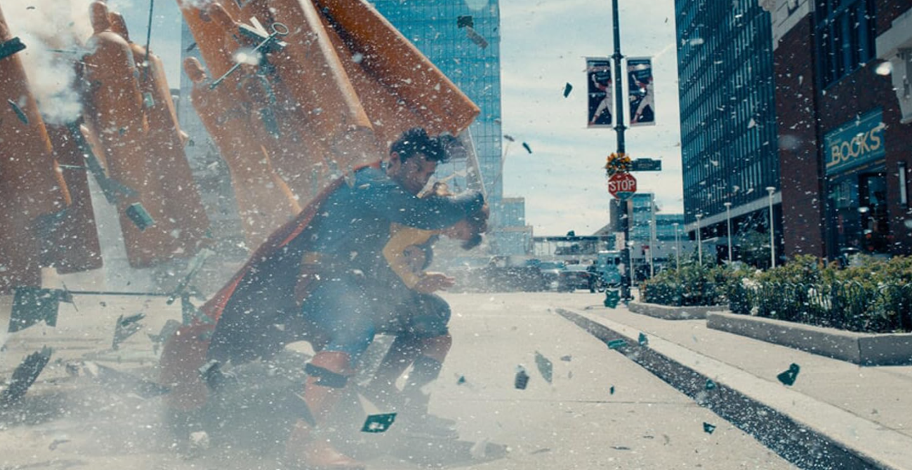 Superman und eine andere Person rennen durch eine Explosion. Gebäude und Trümmer sind im Hintergrund.