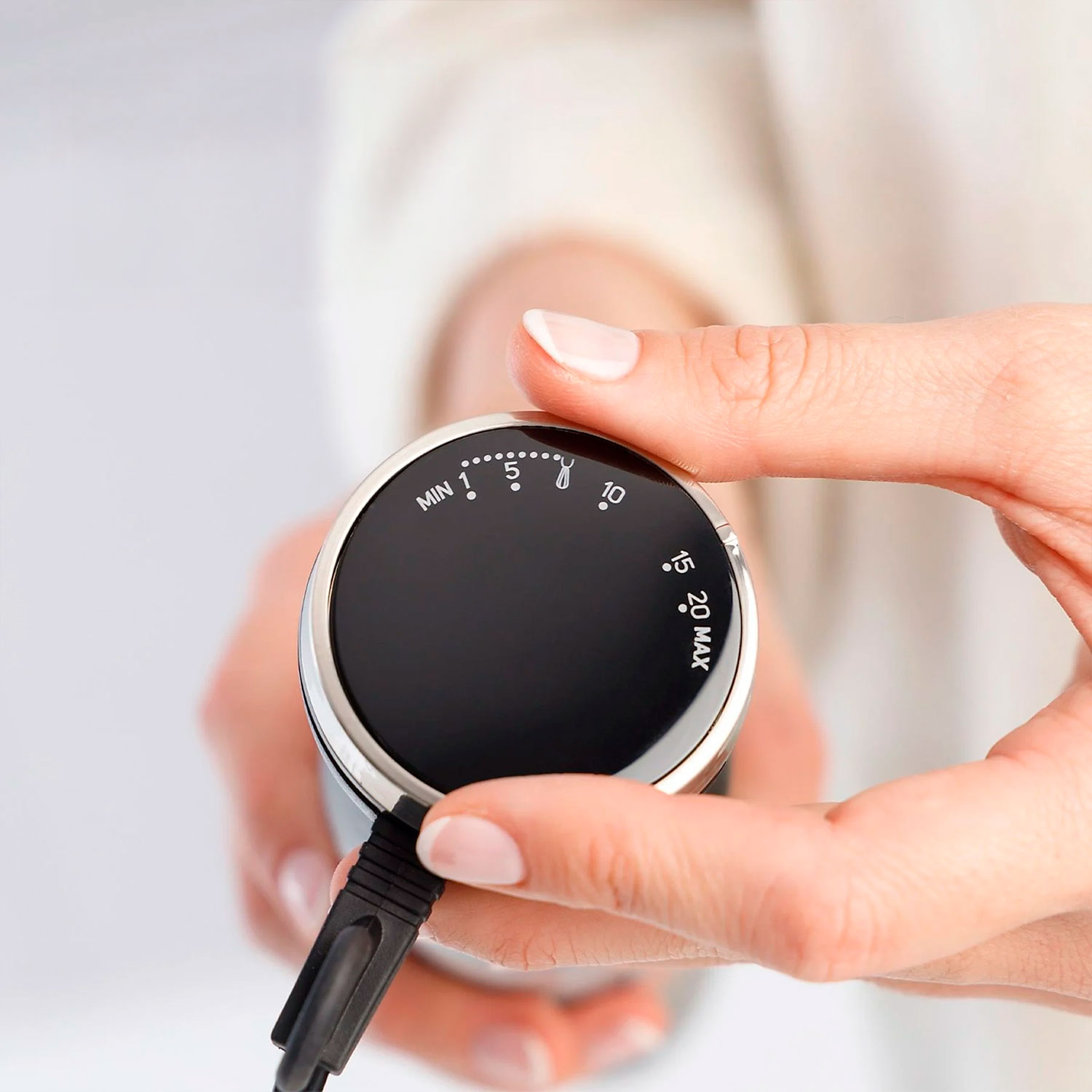 Una mano sostiene un dial negro con números blancos (MIN 1 a MAX 20). El dial es parte de un dispositivo negro con un cable.