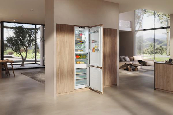 Moderne Küche mit geöffnetem Kühlschrank. Essen drin. Holzschränke und offener Wohnbereich im Hintergrund mit Sofa und großem Fenster.