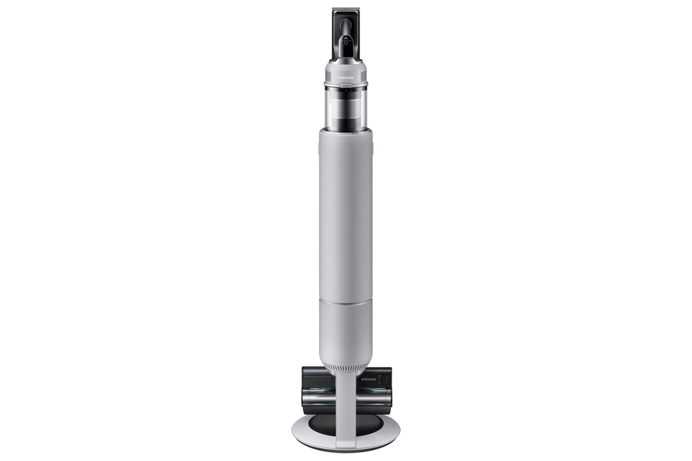 Una aspiradora Samsung gris claro está de pie. Tiene un cuerpo largo y cilíndrico y un cabezal de cepillo en la parte inferior.