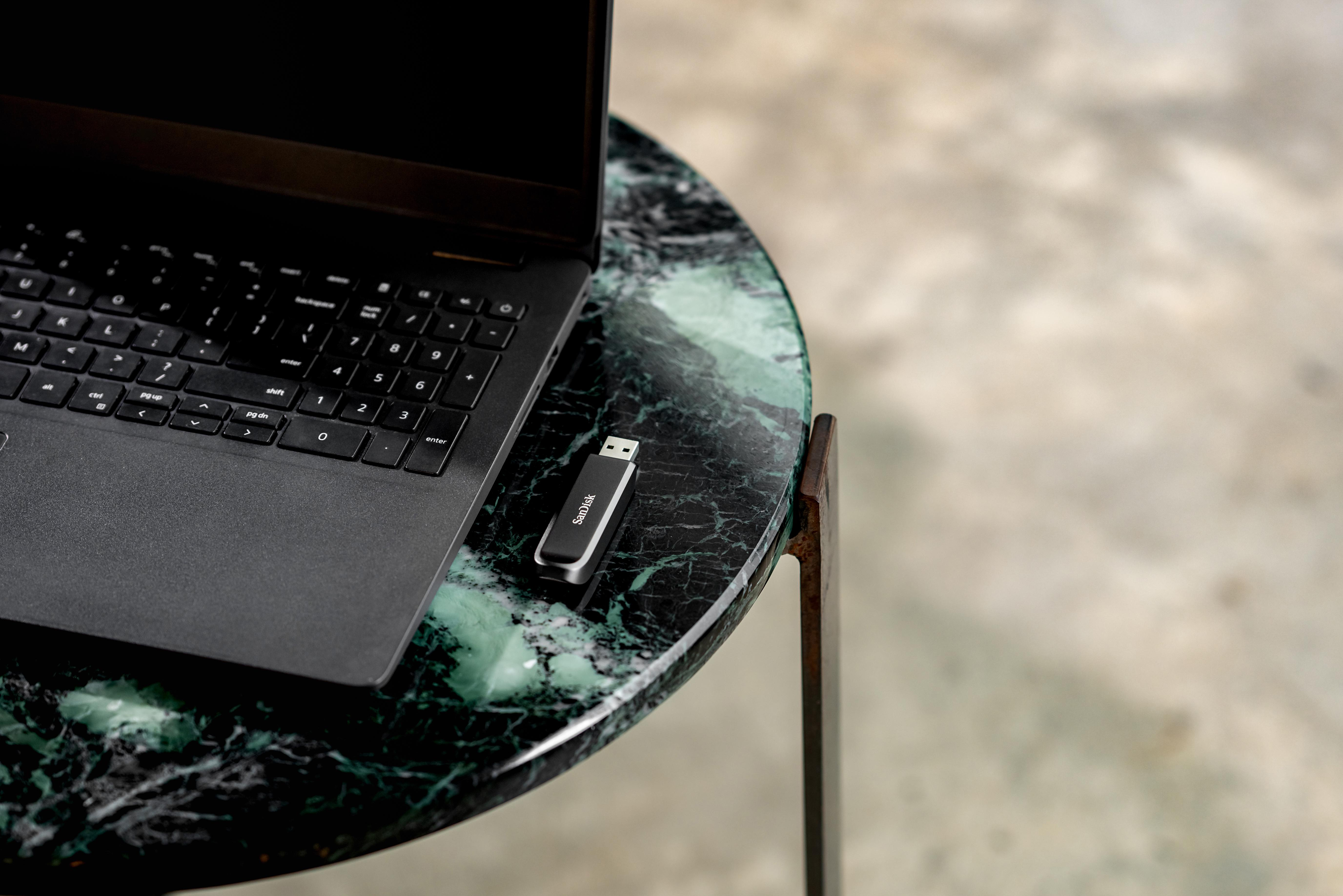 Laptop und USB-Stick auf einem grünen Marmortisch. Tastatur sichtbar. Verschwommener Hintergrund.