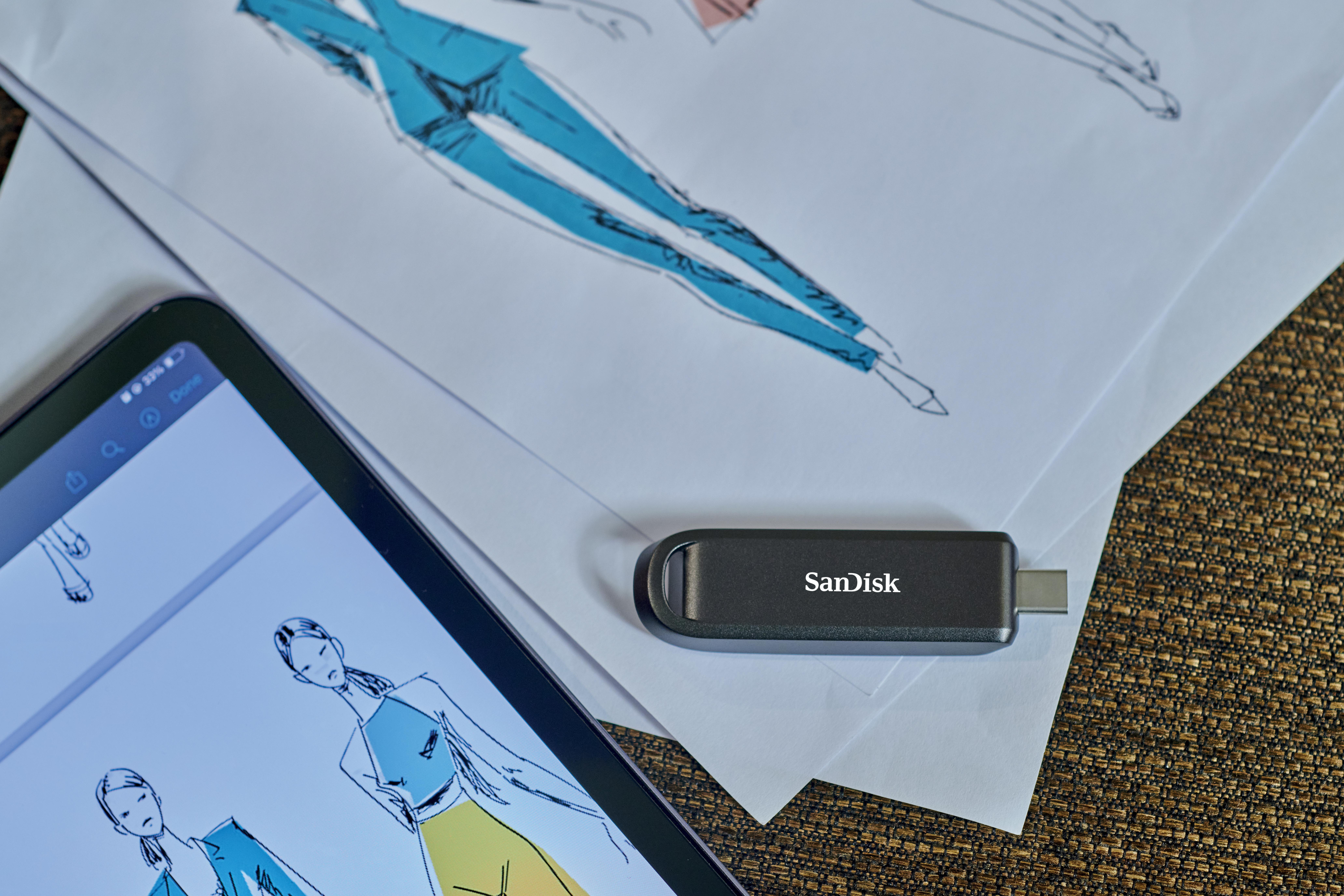 Tablet mit Modeskizzen, SanDisk USB-Stick auf Papier und eine braune, strukturierte Oberfläche.