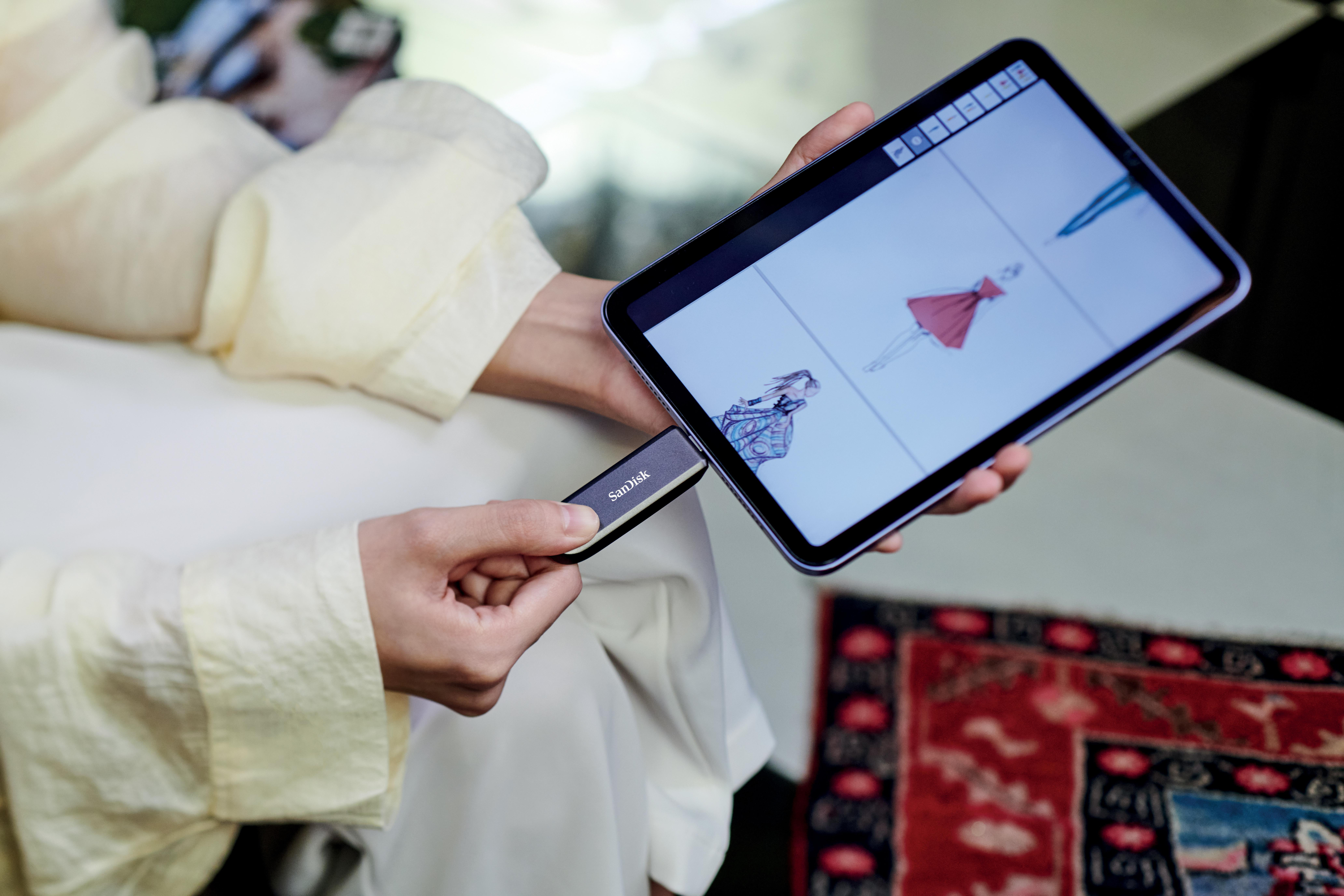 Eine Person hält ein Tablet mit Modeskizzen und einen SanDisk USB-Stick.