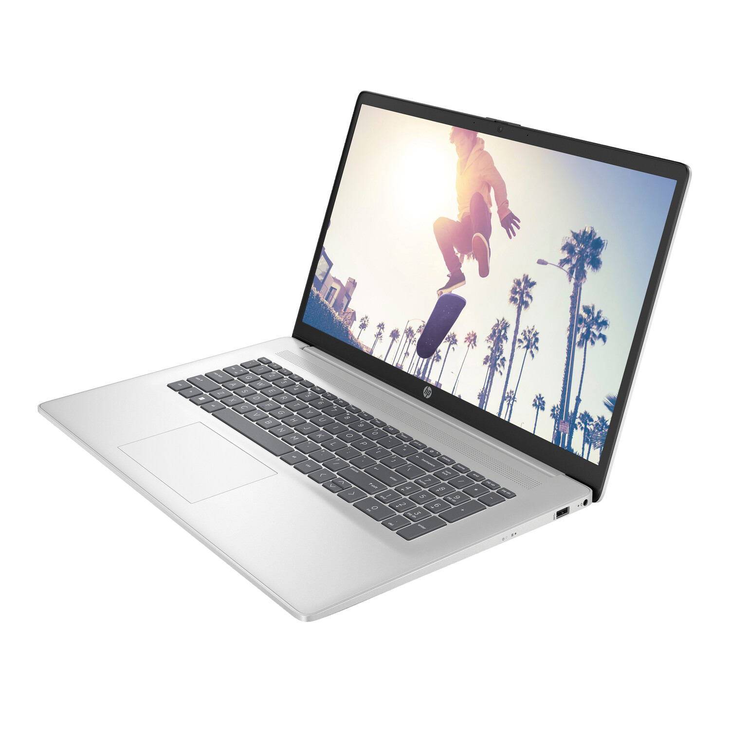 Silver laptop displays a skater in mid-air with palm trees in the background. The laptop is open on a white surface.