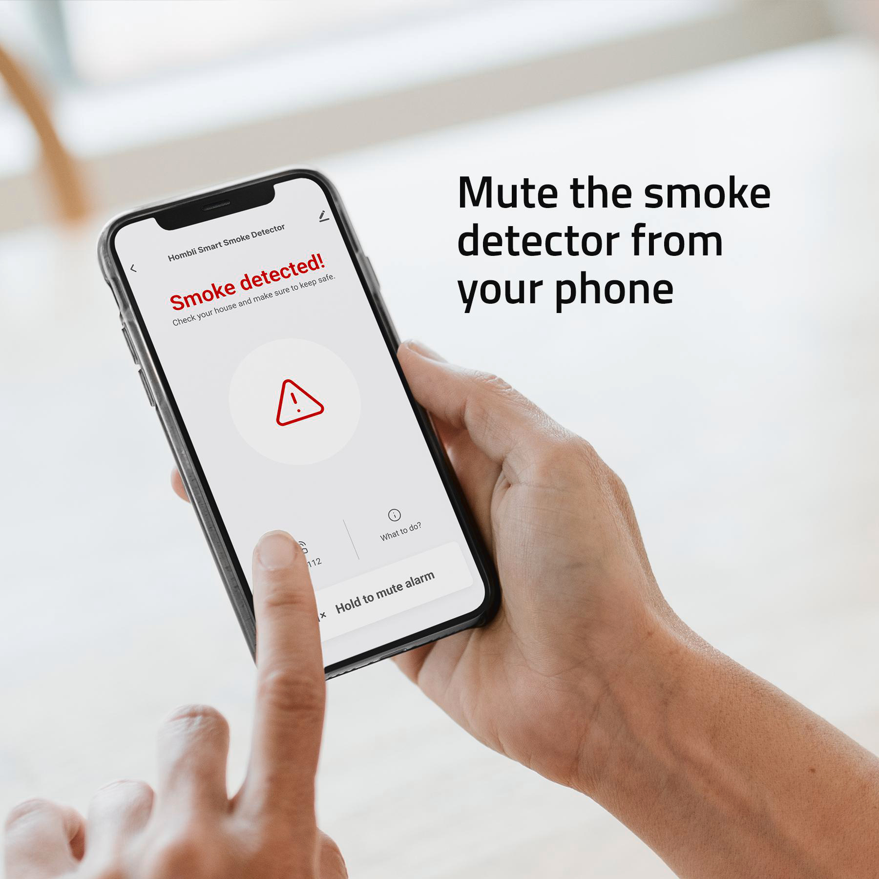Eine Hand hält ein Telefon. Der Bildschirm zeigt 'Rauch erkannt!'. Ein rotes Dreieck mit einem Ausrufezeichen wird angezeigt.