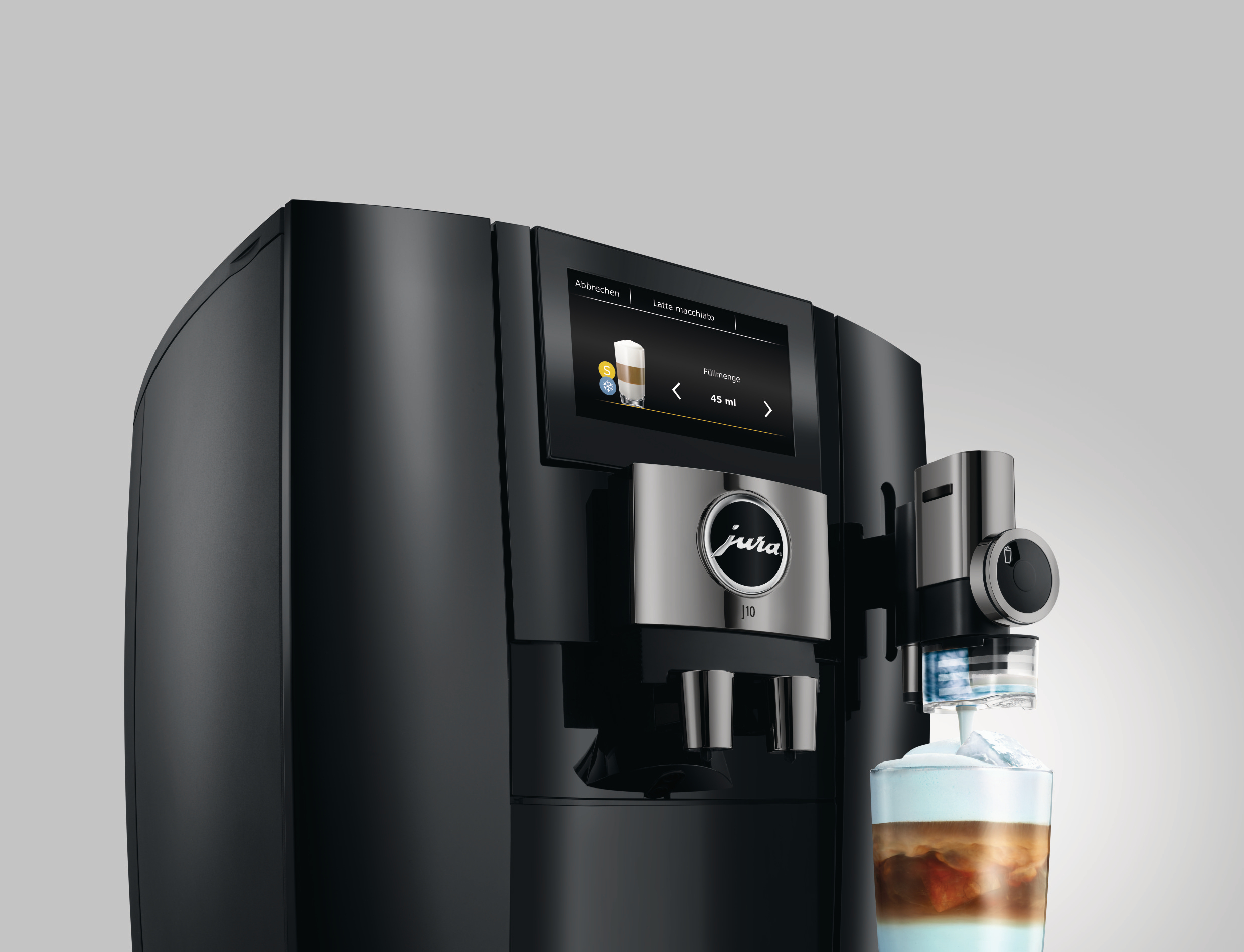 Eine schwarze Jura J10 Kaffeemaschine bereitet einen Latte Macchiato zu. Ein Glas Latte befindet sich vor der Maschine.