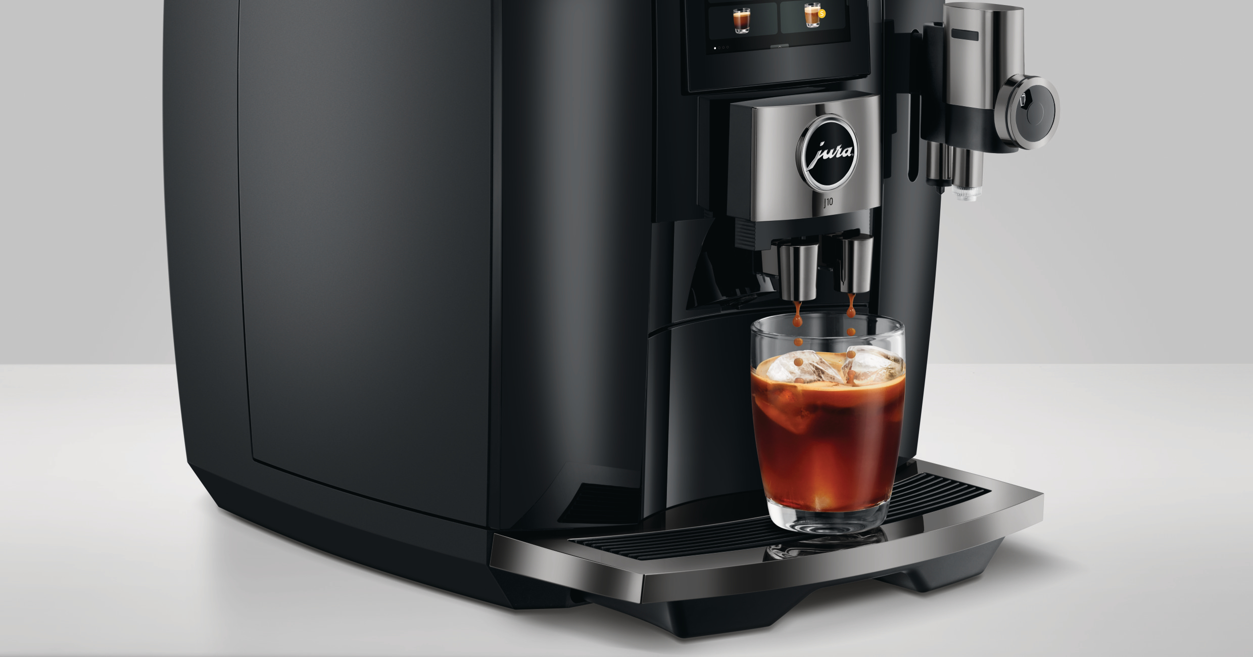 Eine schwarze Jura-Kaffeemaschine, die Kaffee in ein Glas mit Eis abgibt. Die Maschine steht auf einer weißen Oberfläche.