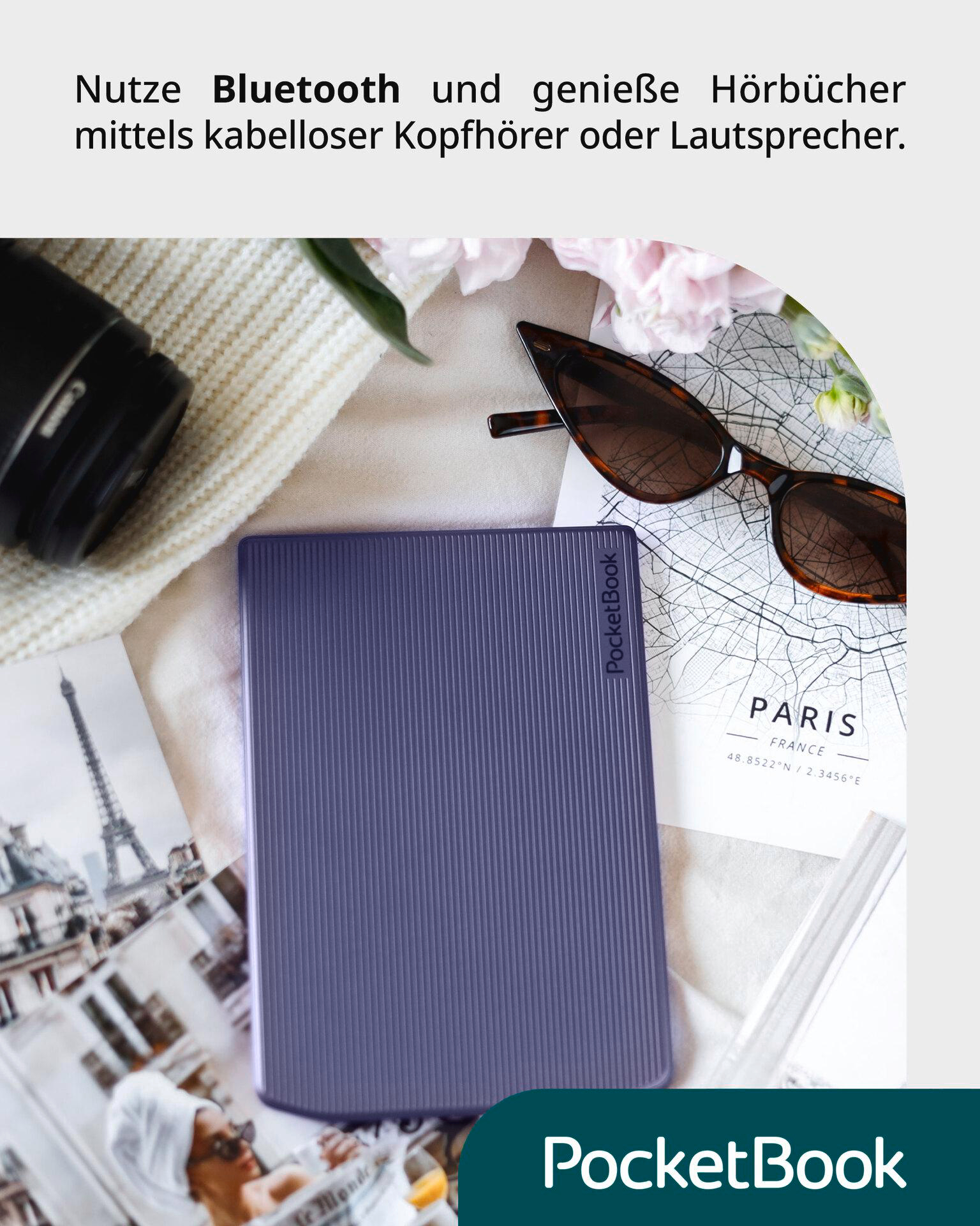Ein lila PocketBook, Sonnenbrille, eine Karte von Paris und eine Kamera liegen auf einer hellen Oberfläche, was auf ein Reisetema hindeutet.
