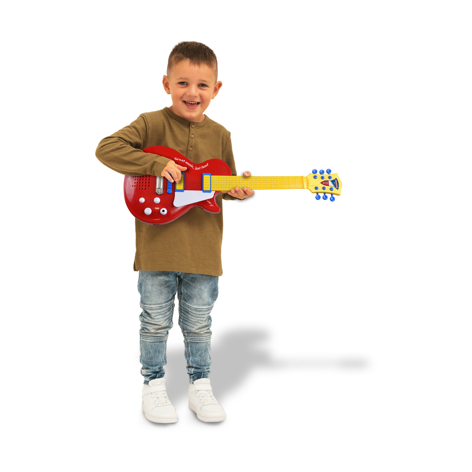 Un ragazzo tiene una chitarra giocattolo rossa e gialla. Indossa una maglietta verde, jeans blu e scarpe da ginnastica bianche. Sorride.