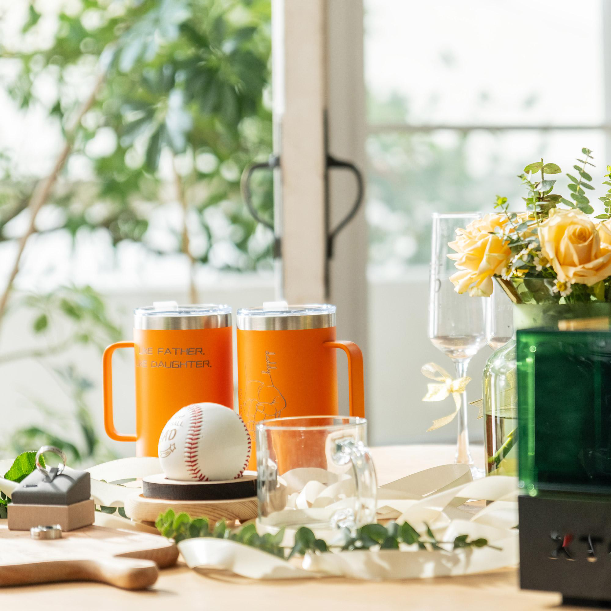 Tisch mit orangefarbenen Tassen, Baseball, Blumen, Sektgläsern und einer grünen Box. Eine Ringbox und Grünzeug sind ebenfalls vorhanden.