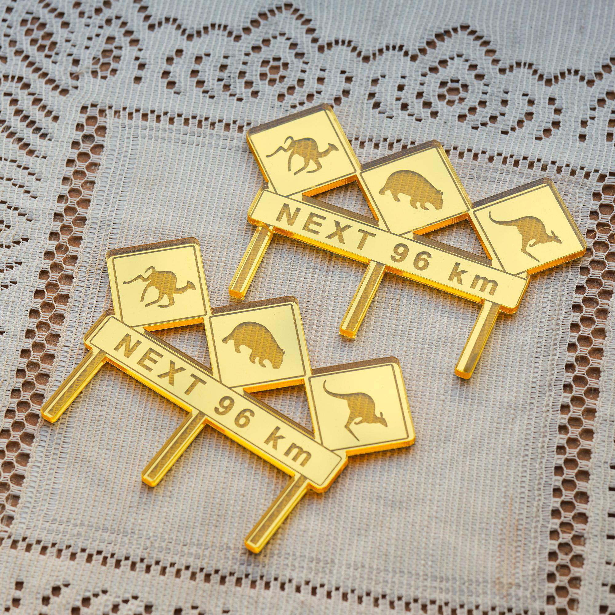 Goldene Schilder mit Tiersilhouetten und 'NEXT 96 km' auf gemustertem Stoff.