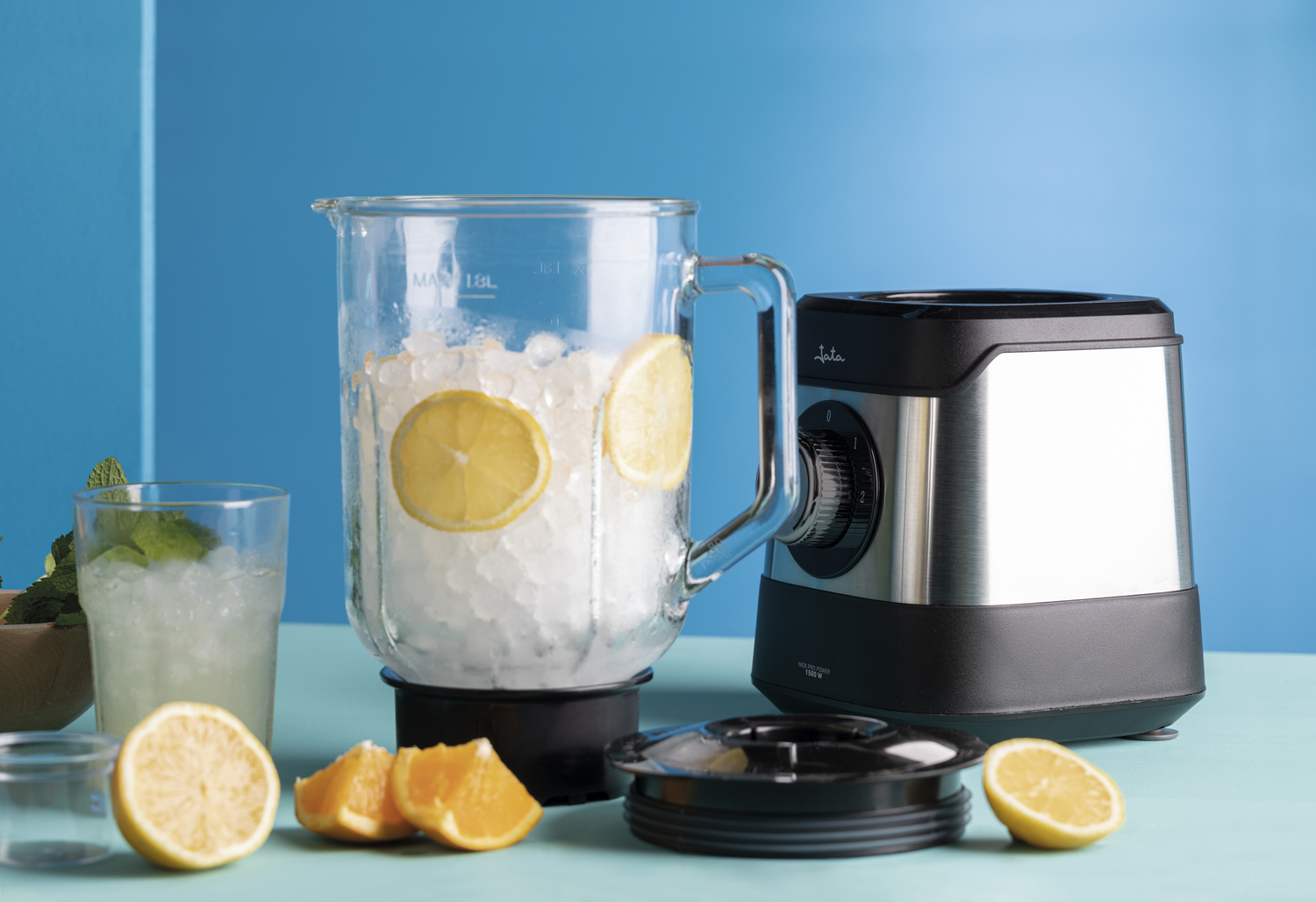 Licuadora con hielo, limones y naranjas. Se prepara una bebida. Fondo azul y superficie azul claro.
