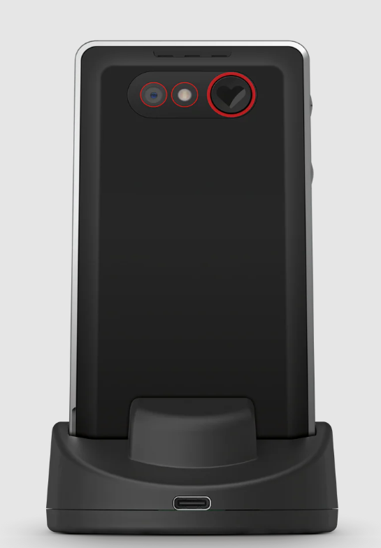Schwarzes Telefon auf einer schwarzen Ladestation. Das Telefon hat Kameralinsen und eine herzförmige Taste. Der Hintergrund ist hellgrau.