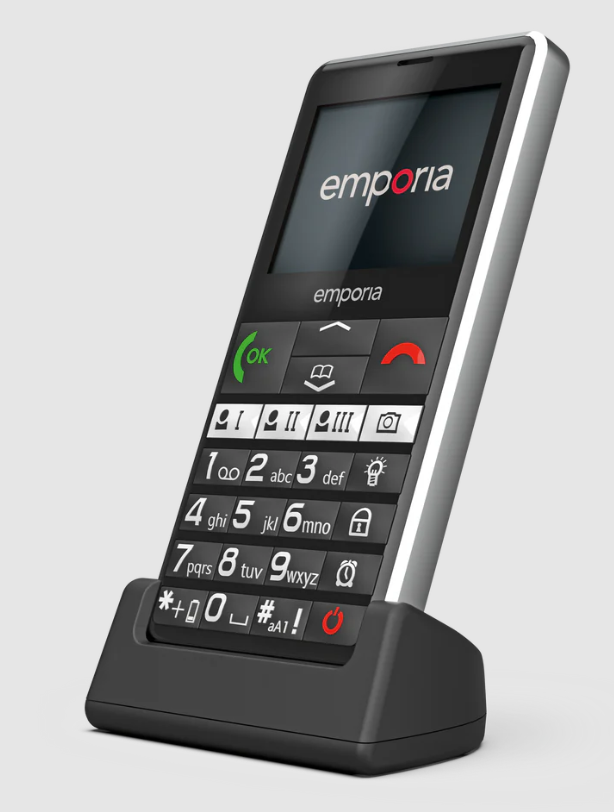 Ein schwarzes Emporia-Telefon in seiner Ladestation. Es hat große Tasten und einen Bildschirm mit dem Markennamen.