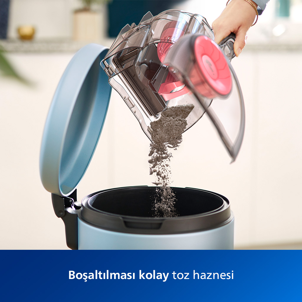 Bir kişi, bir elektrik süpürgesinin toz kabını açık mavi bir kutuya boşaltıyor. Gri toz kutuya düşüyor. Kutu kırmızı bir filtreye sahip.