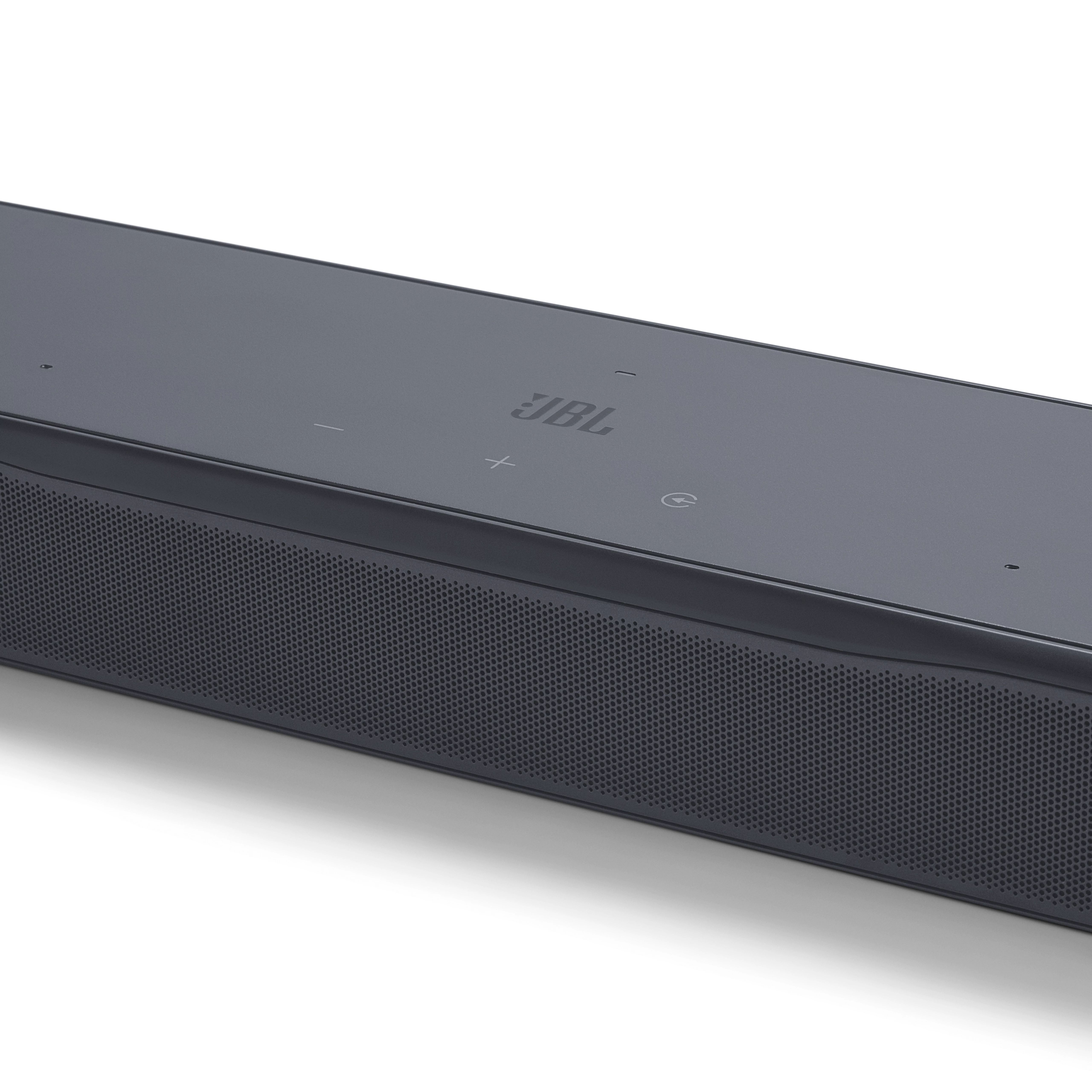 Beyaz zemin üzerinde koyu gri JBL soundbar. JBL logosu, ses ve güç düğmelerini içerir.